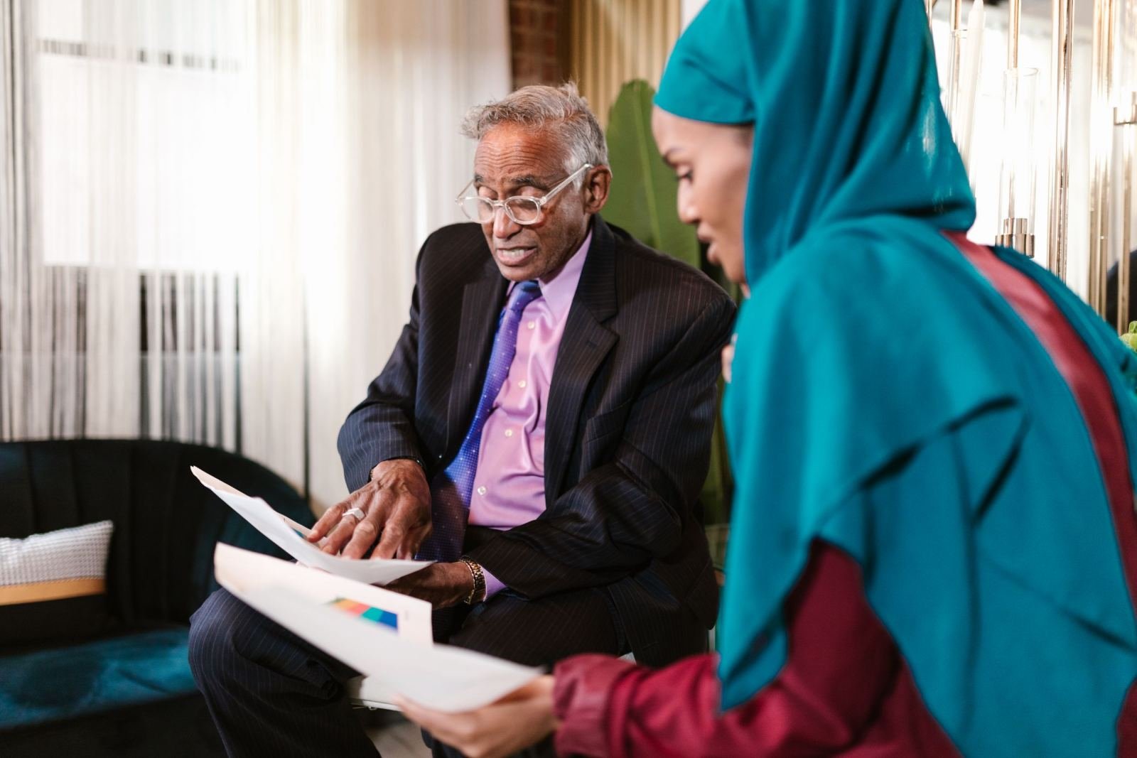 A woman wearing a teal hijab and a man in a suit look over paperwork together.