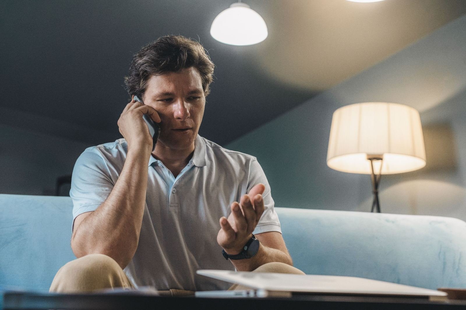 A man sits on a sofa talking on his cell phone. A notebook rests close by.