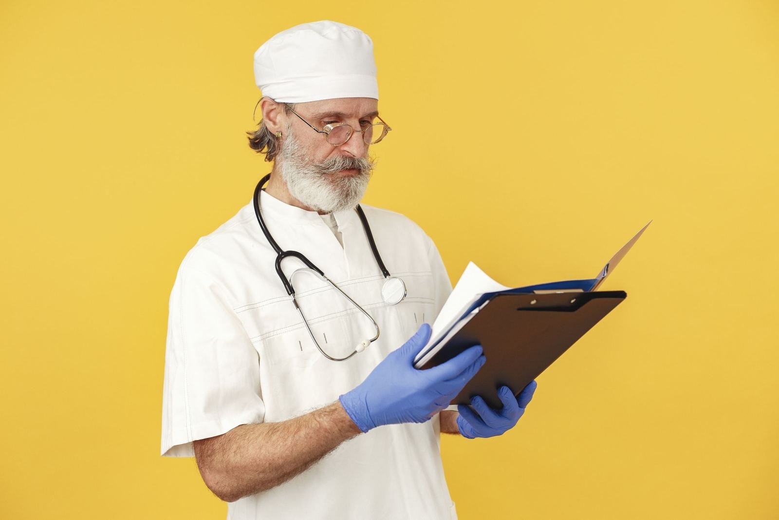 A clinician wearing blue gloves and a white coat looks at a clipboard.