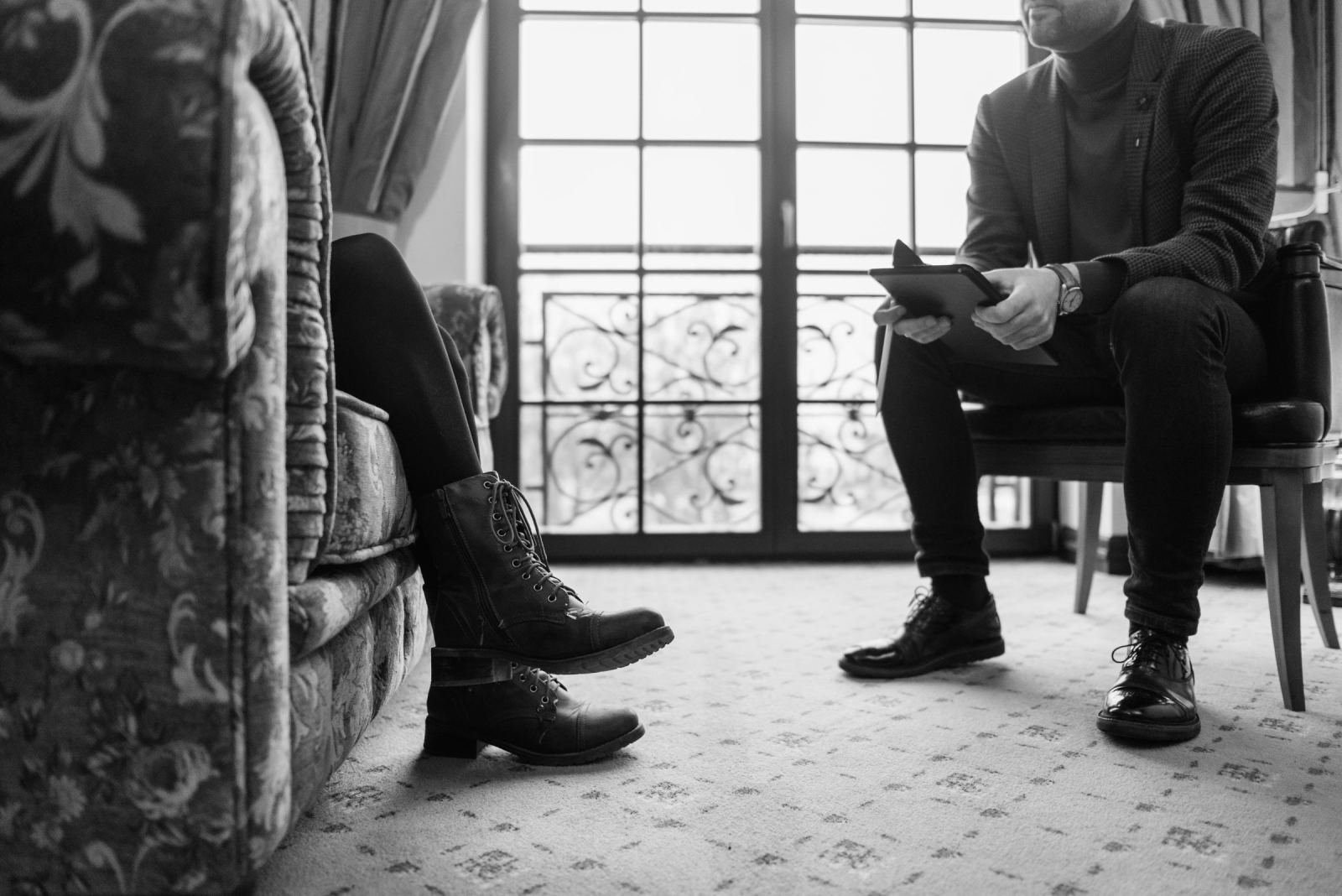 Two people sit opposite each other in a room, one holding a notebook