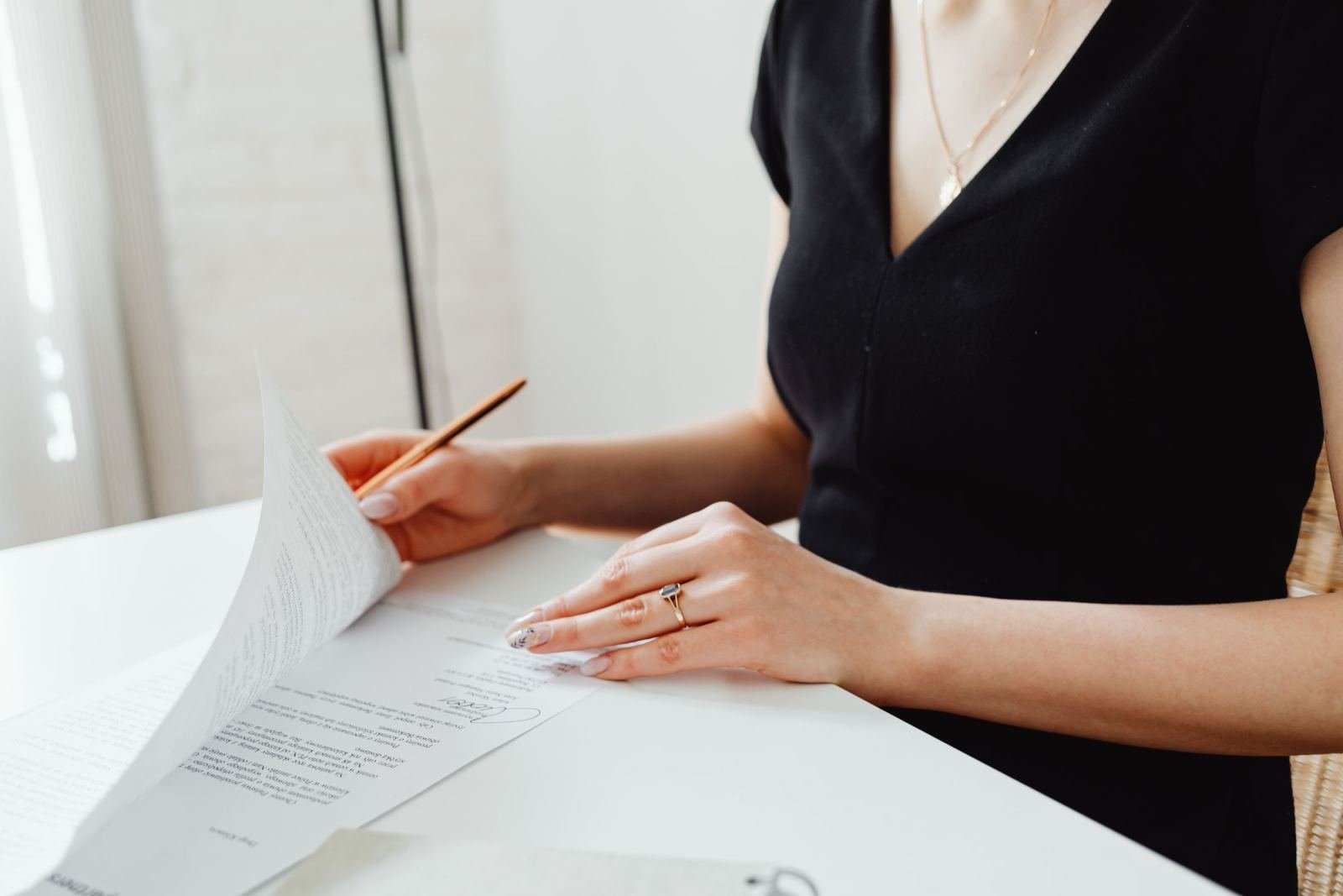 A person at a white desk reviews a printed document with a pencil