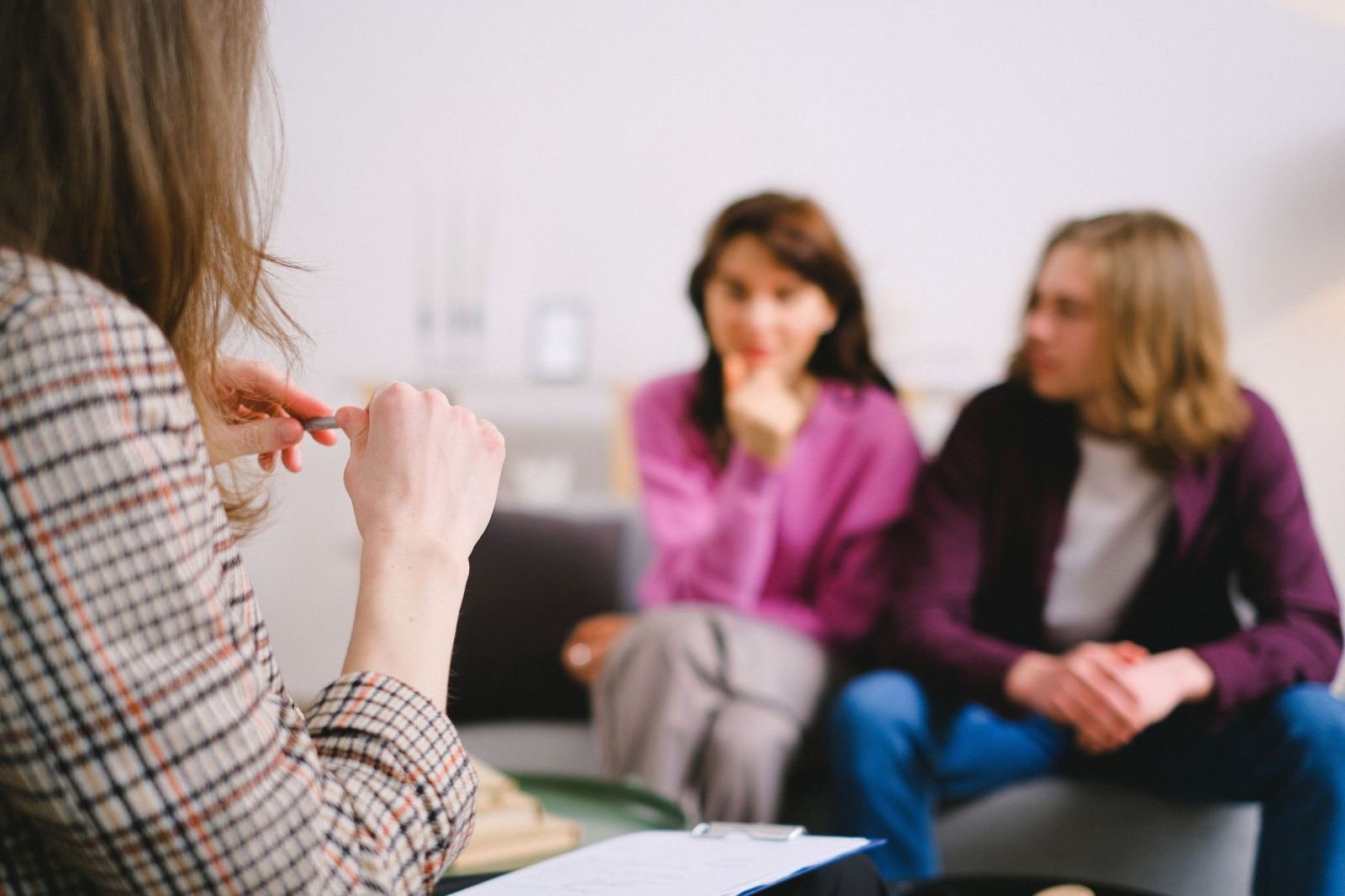 A professional in a plaid blazer talks with a couple on a sofa