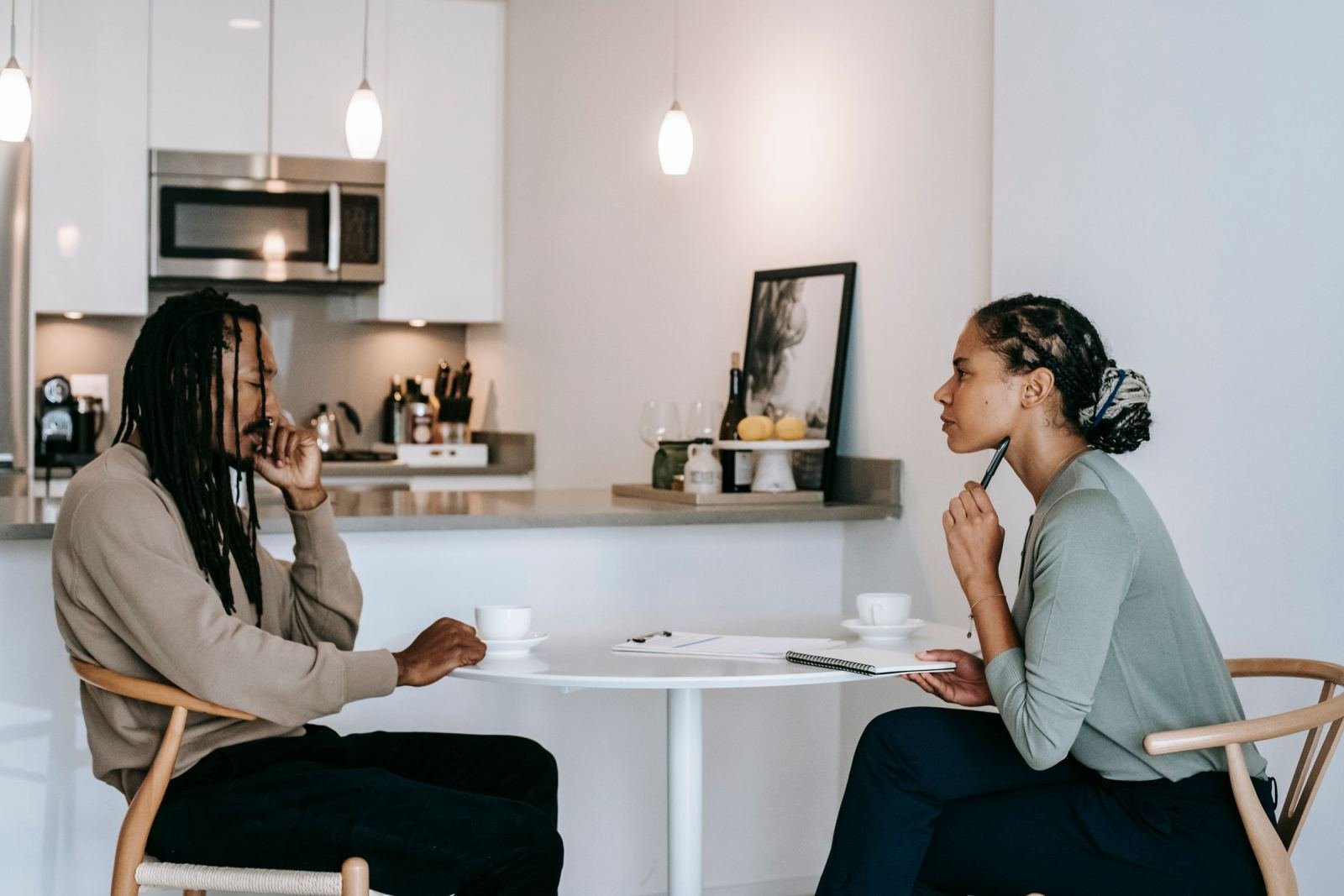 In a bright room, a man and a woman talk at a white table