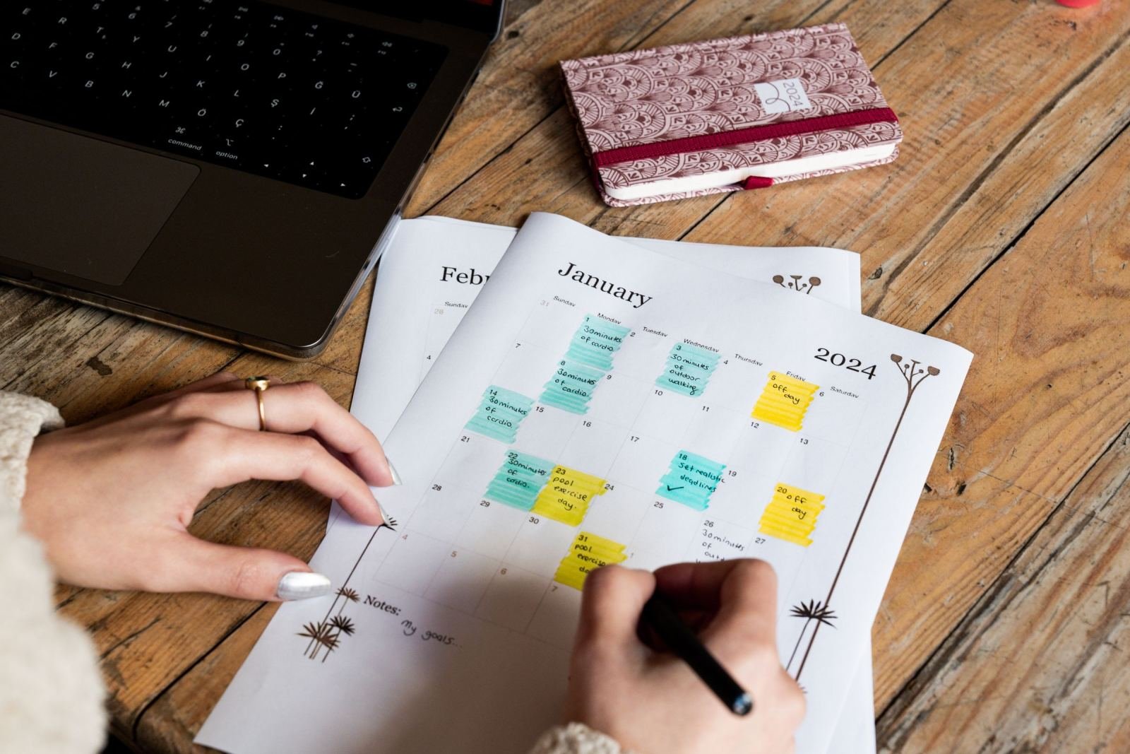 A close-up of hands placing bright sticky notes on a January 2024 calendar.