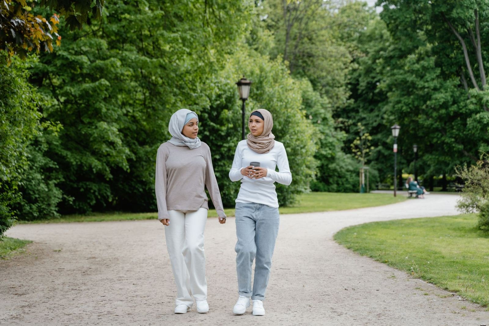 Two women in hijabs chat as they walk along a path in a park