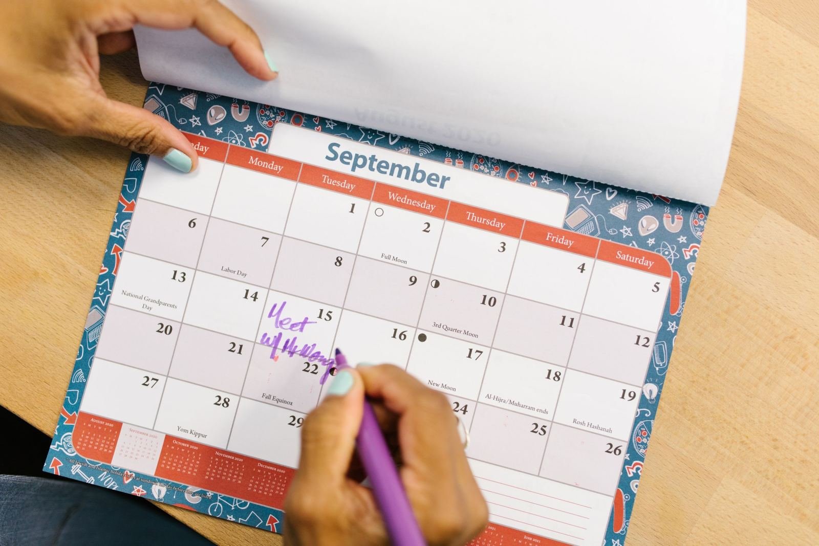 A person uses a purple marker to write an appointment on a September calendar