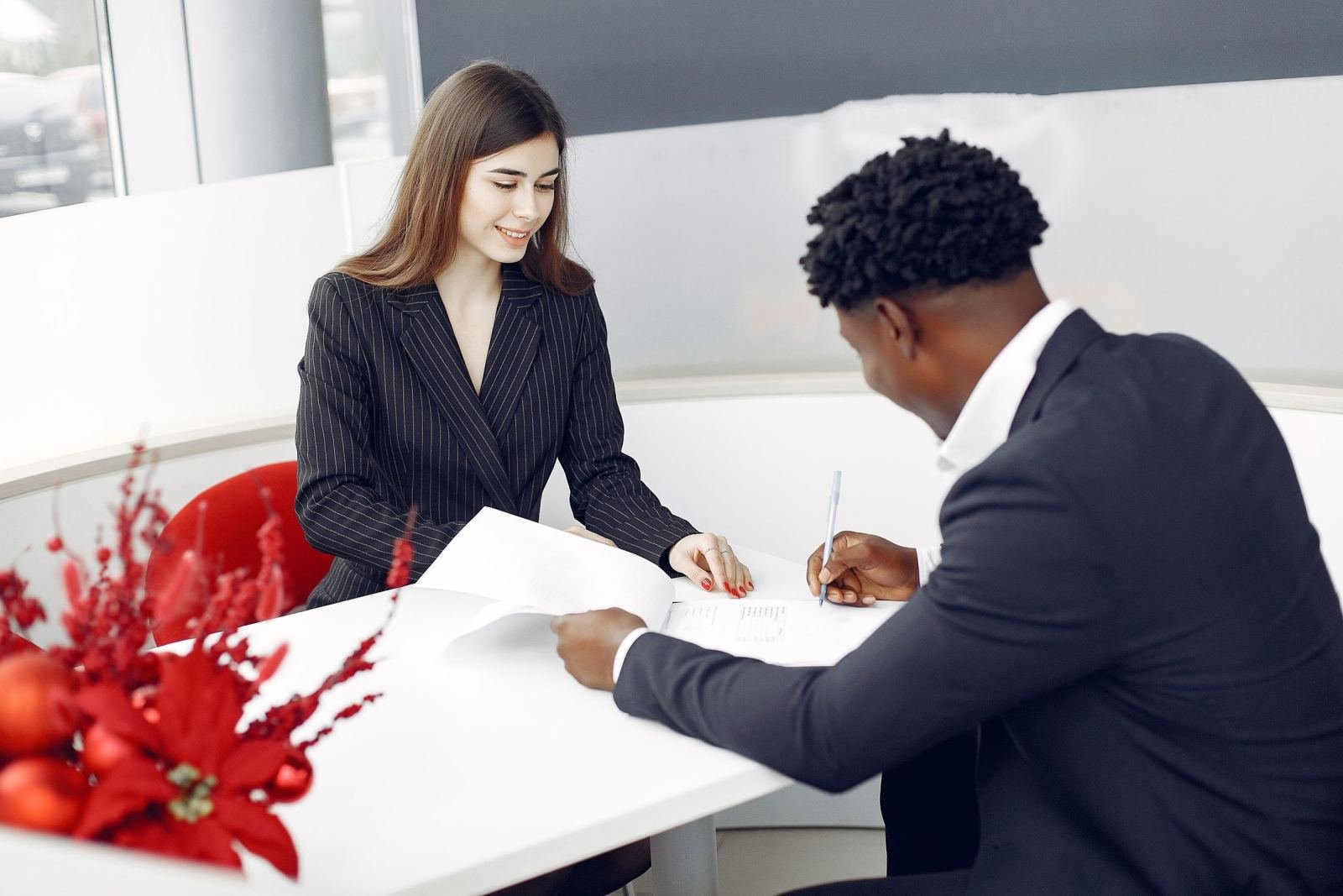 A woman in a blazer and a man in a suit review a notebook at a white table