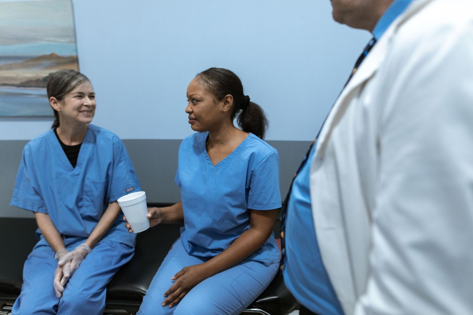 Two medical professionals in blue scrubs talk in a clinic