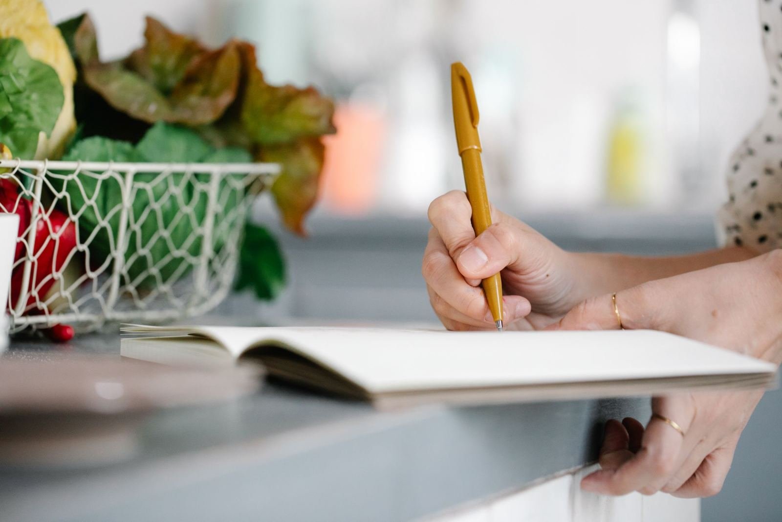 A person using a yellow pen to write in a notebook on a kitchen counter