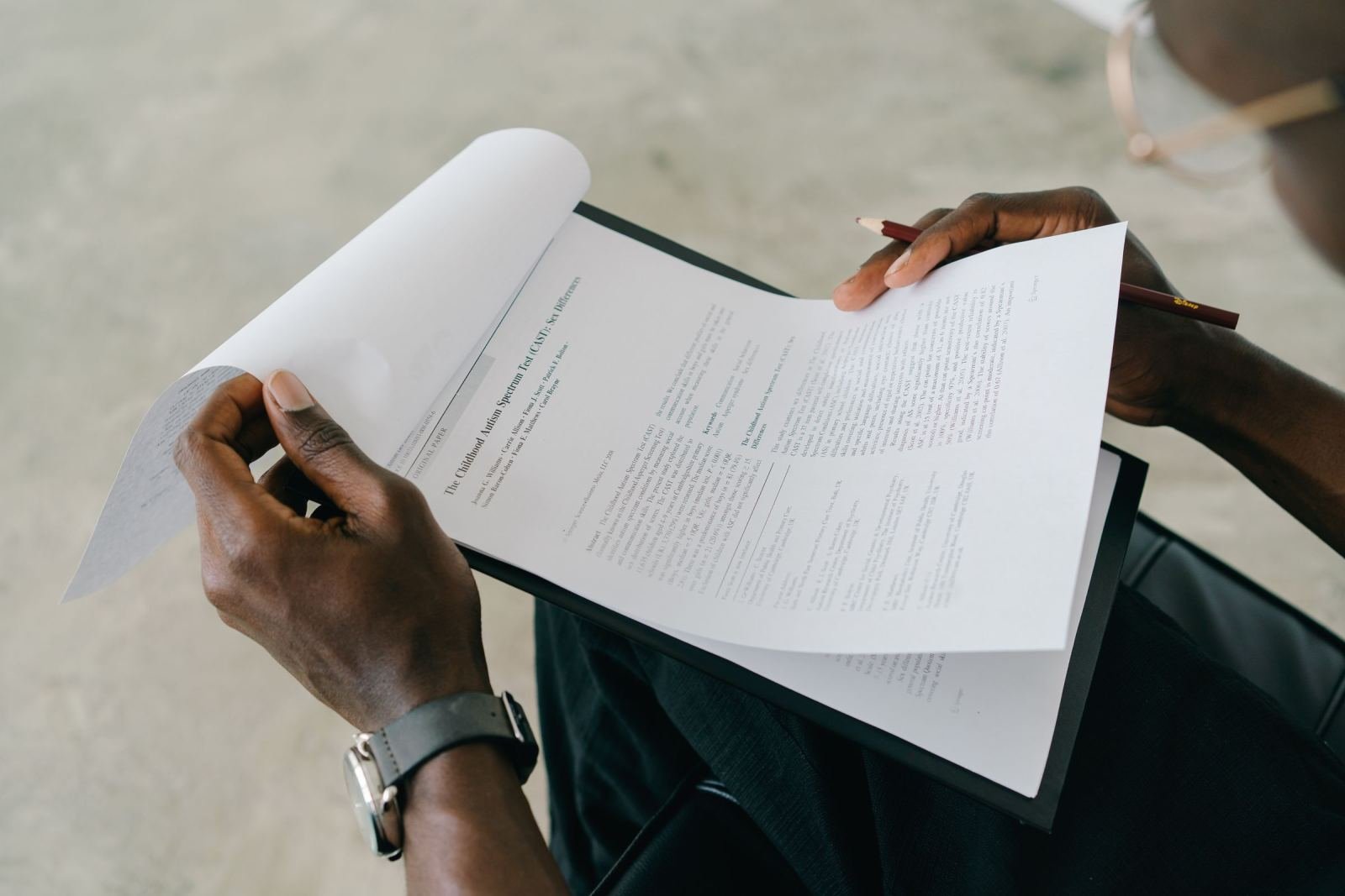 Hands hold a clipboard while a page of a printed paper is turned.