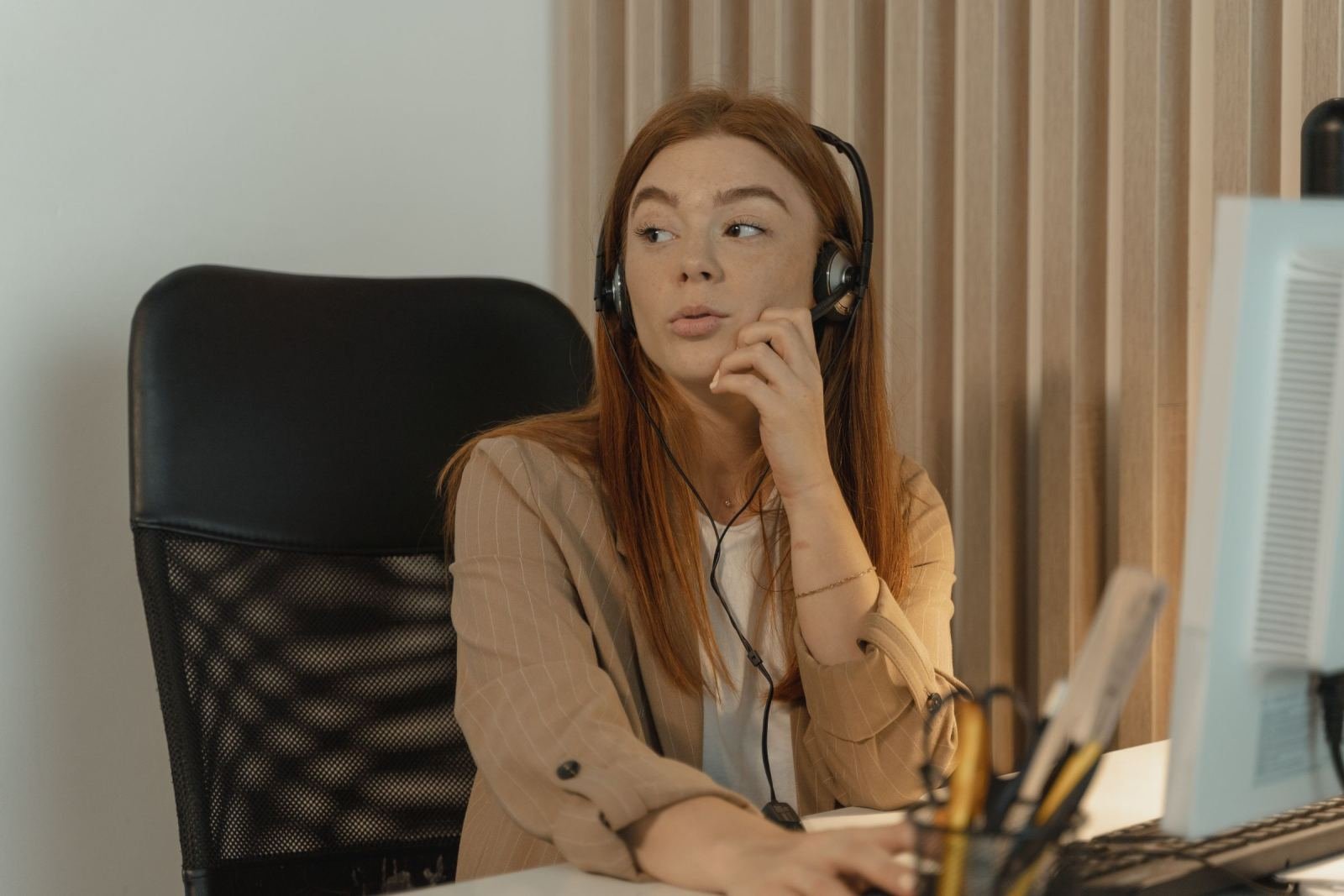 A woman wearing a headset sits at a computer desk and looks to the side