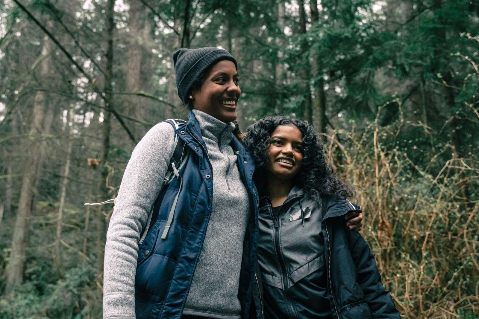 Two women smiling and walking together through a wooded area