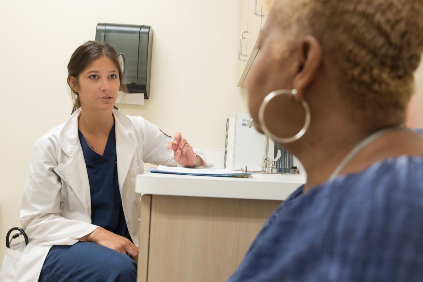 A doctor in a white coat talks to a patient in a clinic.