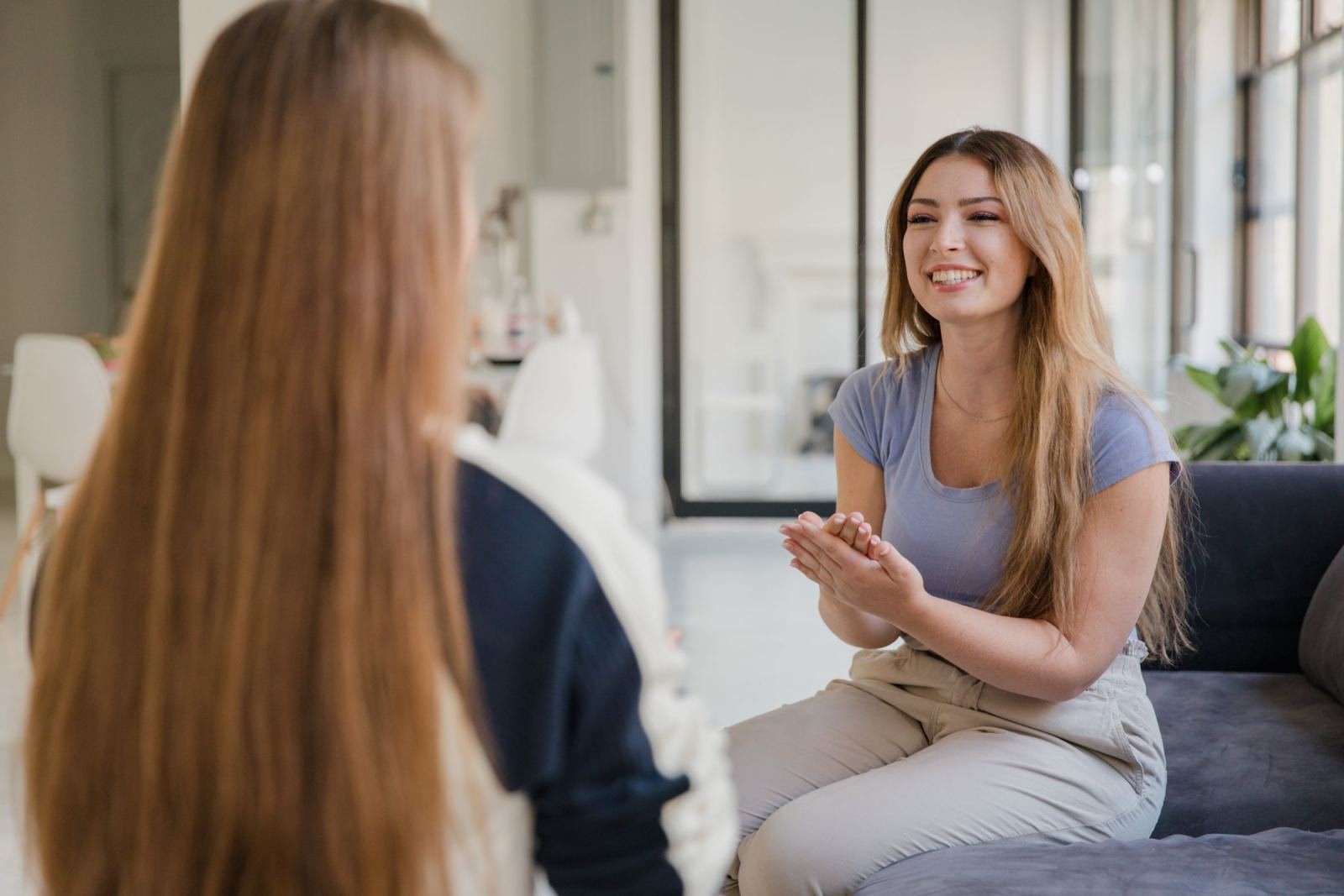 A smiling woman sits on a sofa and talks with another person in a bright office