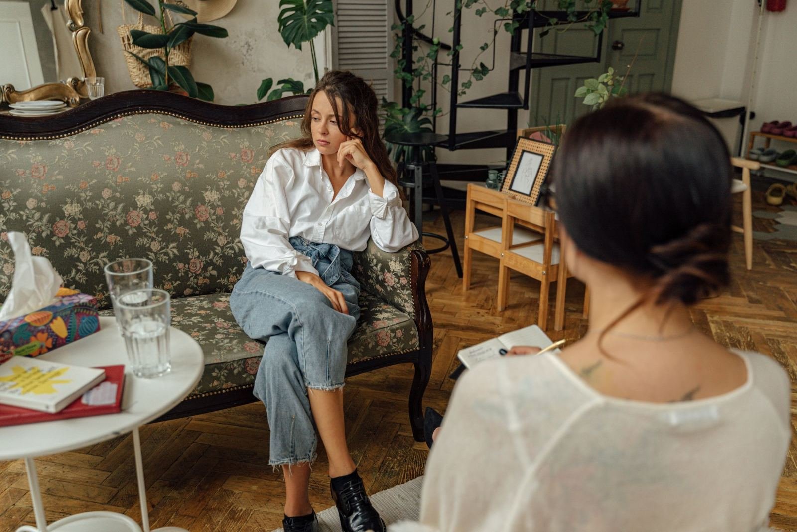 A woman in a floral sofa talks with a counselor who holds a notebook
