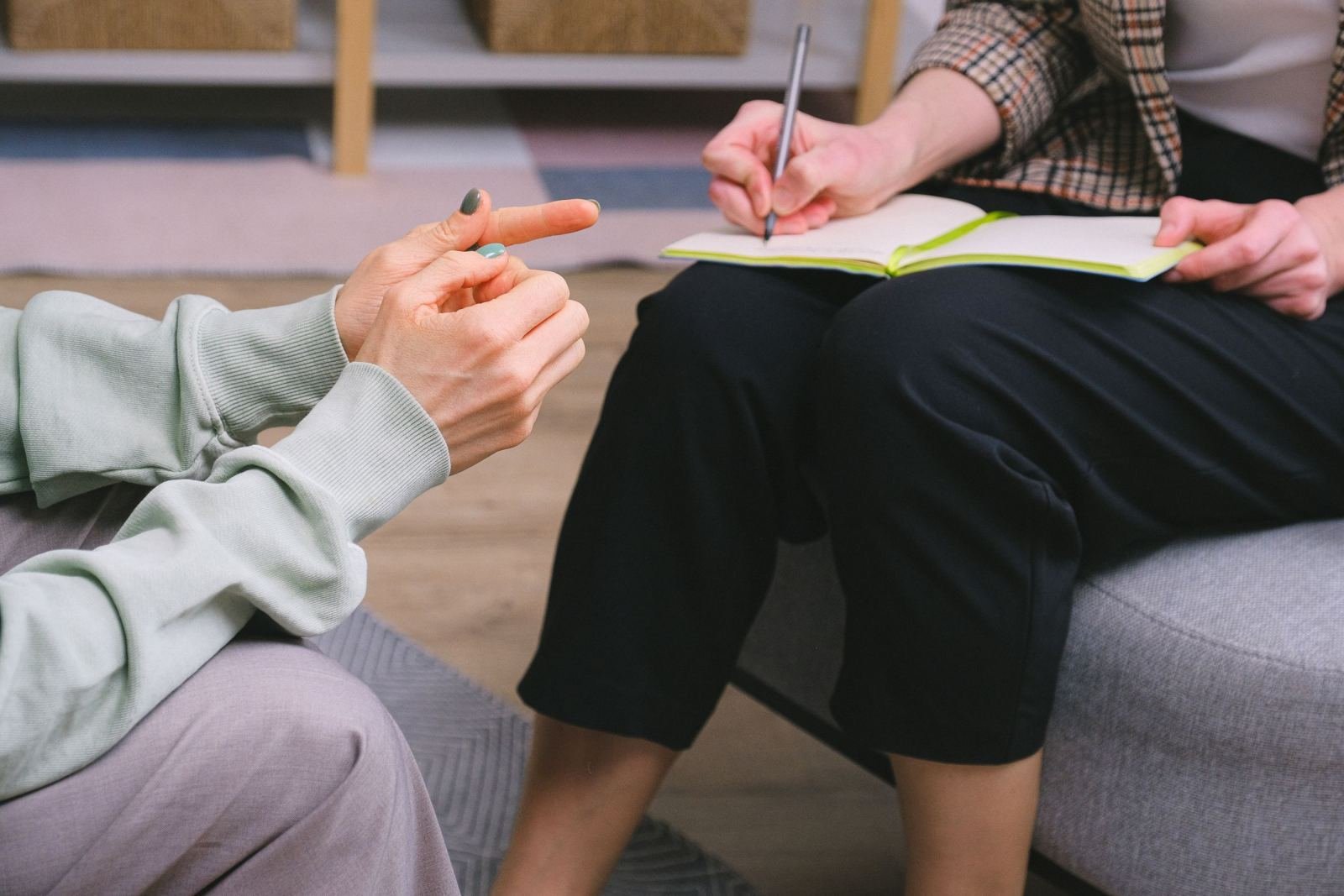 One person writes in a notebook while a second person uses hand gestures to talk.