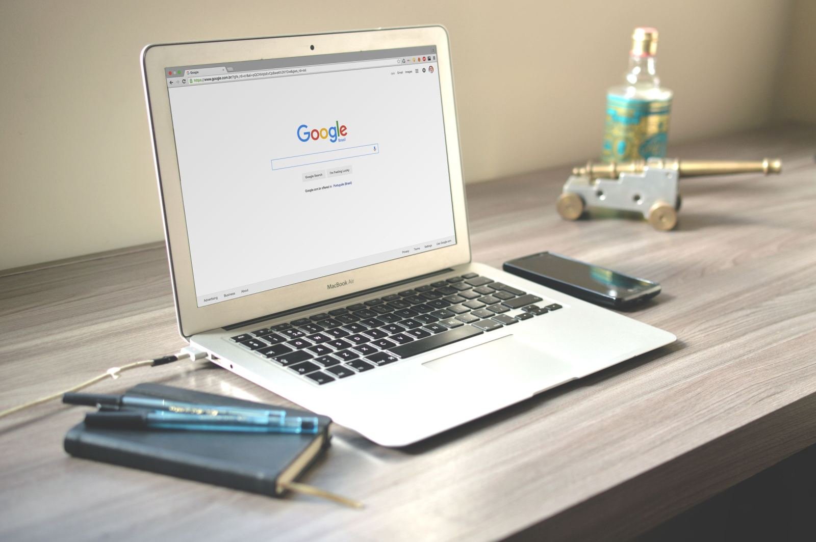 An open laptop showing a search engine on a wooden desk with a phone and notebook
