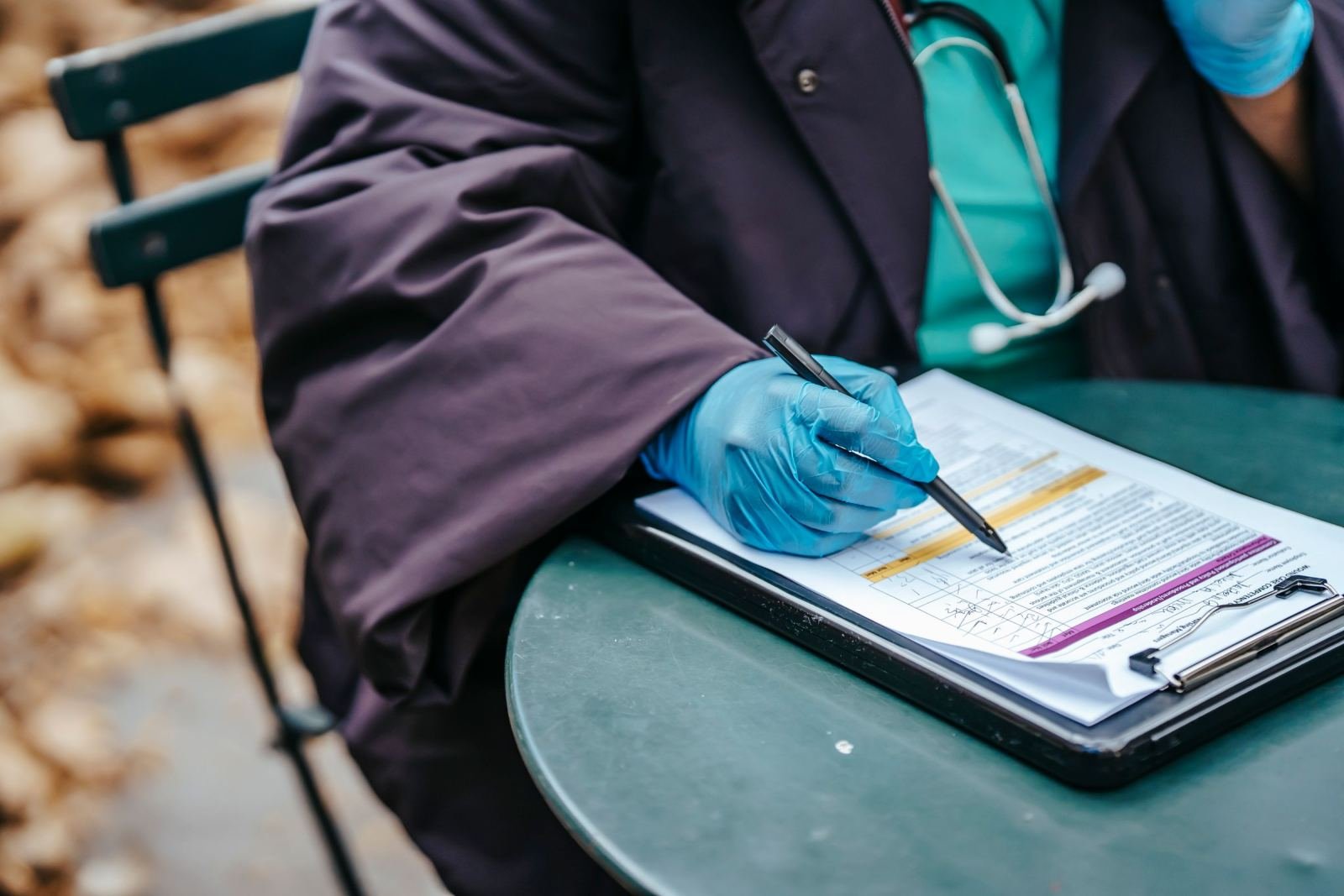 A medical professional in blue gloves writes on a clipboard at a green table