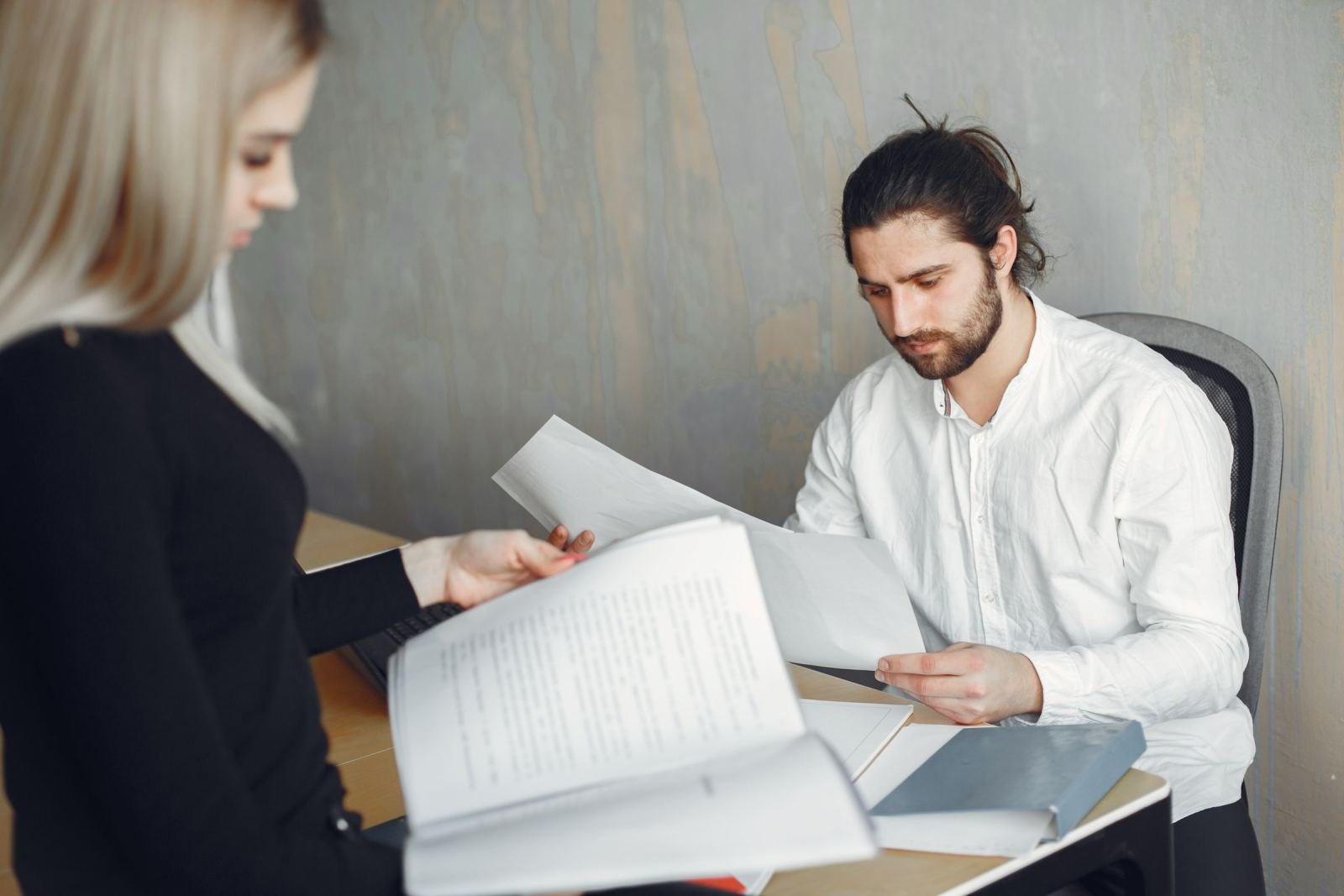 A man and a woman sit at a desk looking at printed papers.