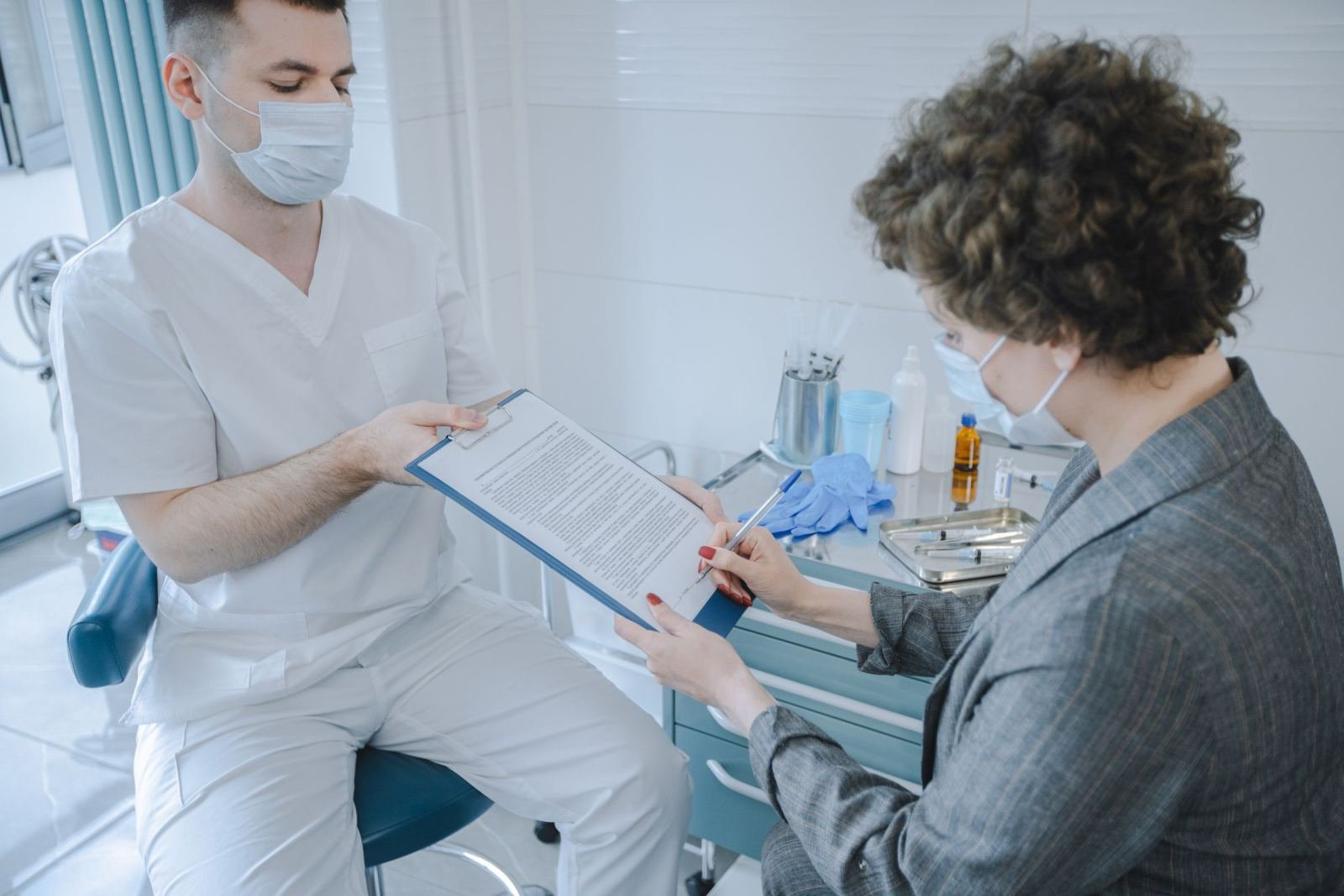 A clinician in a mask and scrubs shows a document on a clipboard to a woman