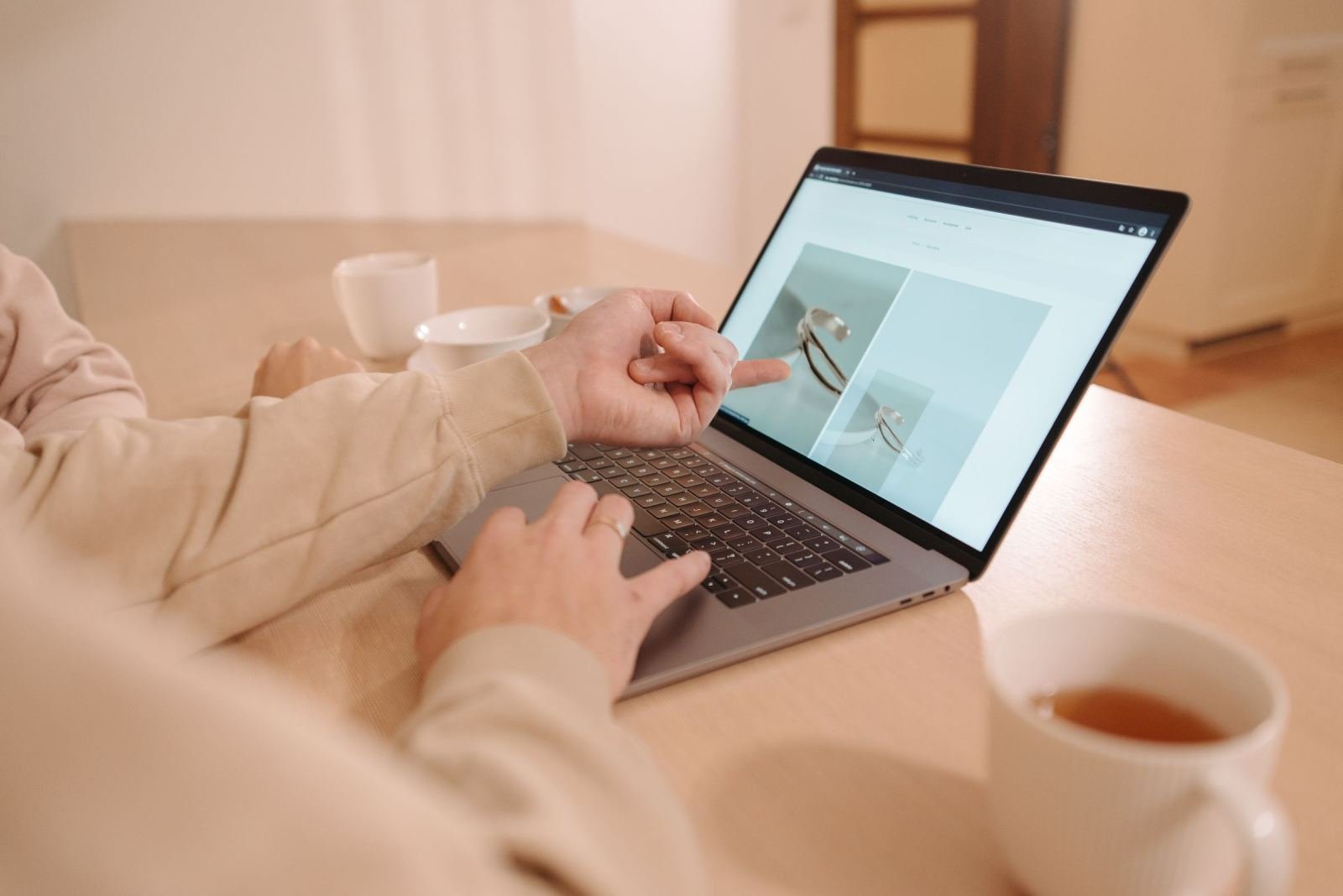 A pair of people share a laptop screen while sitting at a wood table.