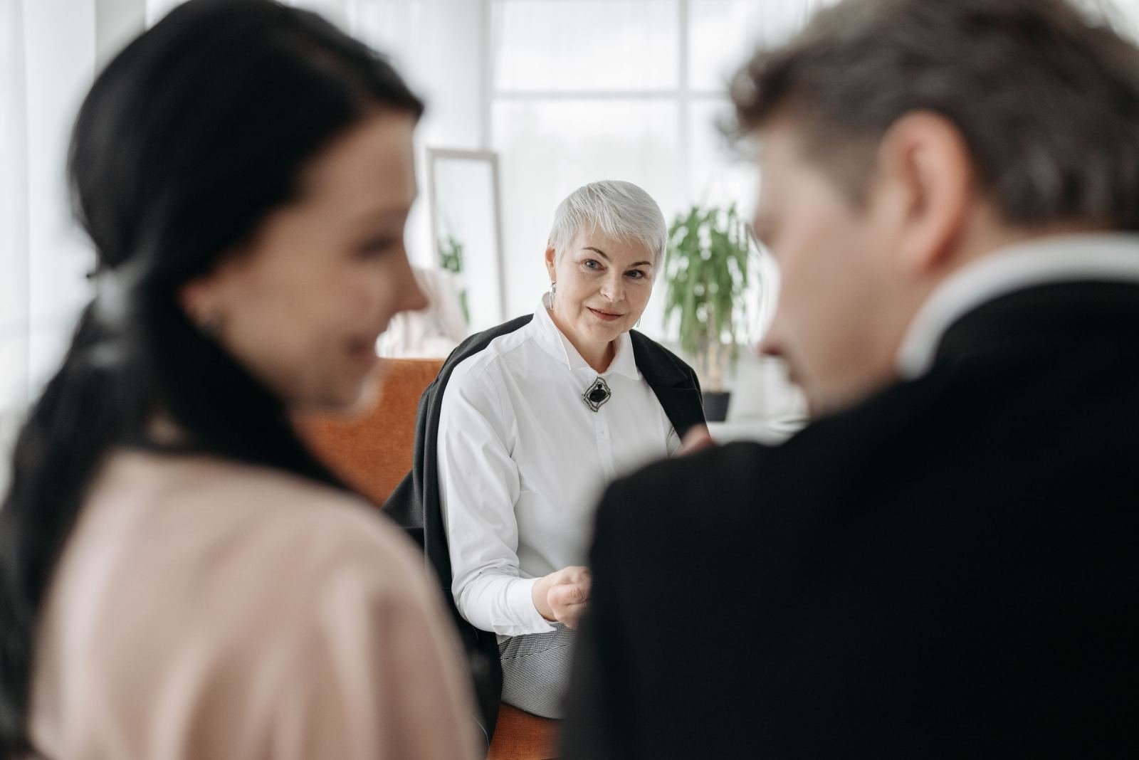 A woman in a white shirt talks to a couple in a bright office.
