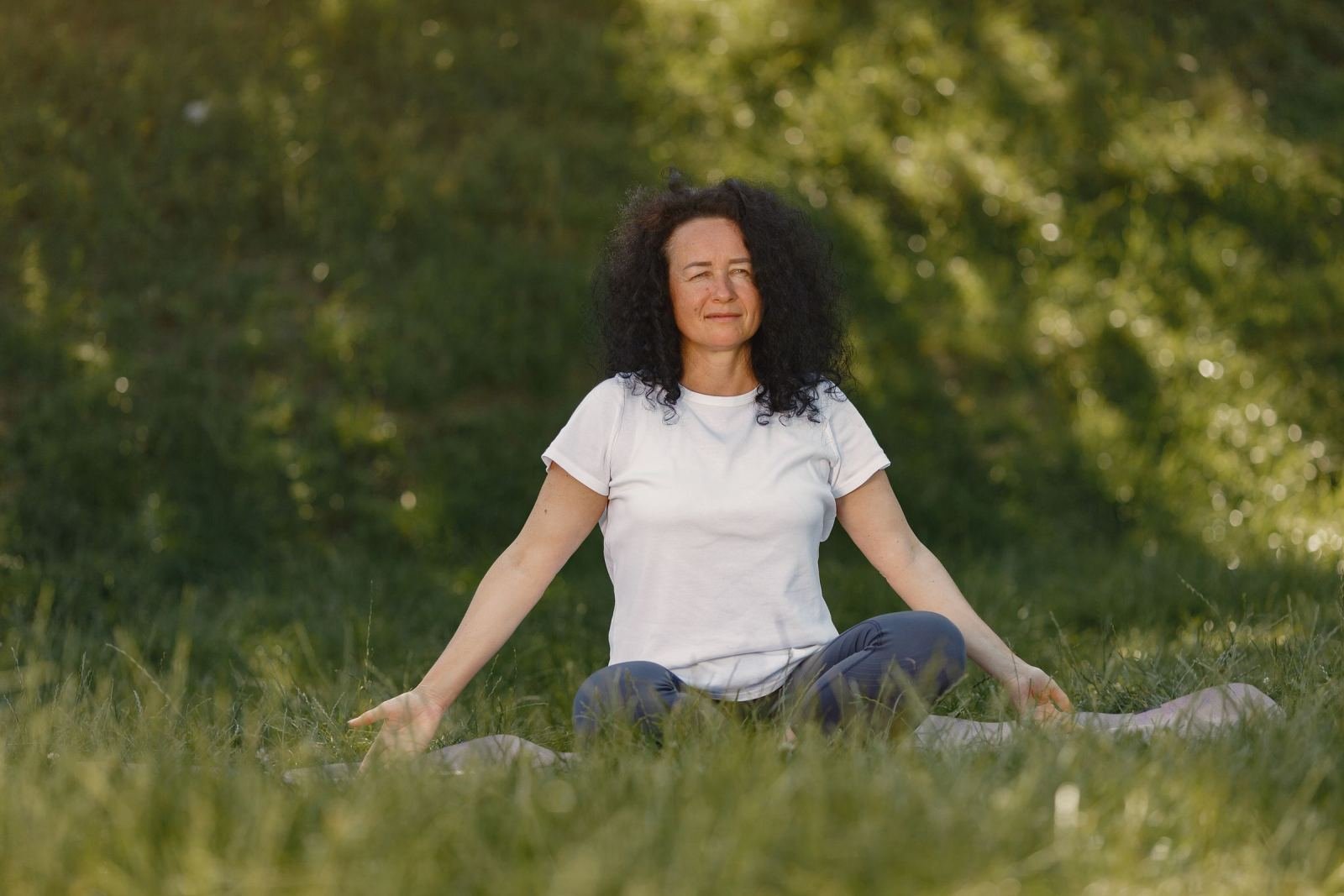She sits in the grass with her legs crossed and her eyes shut.