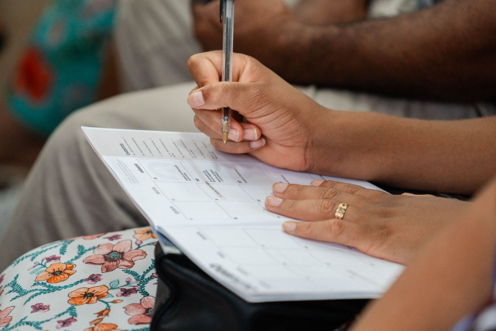 A person uses a pen to mark a date on a printed calendar