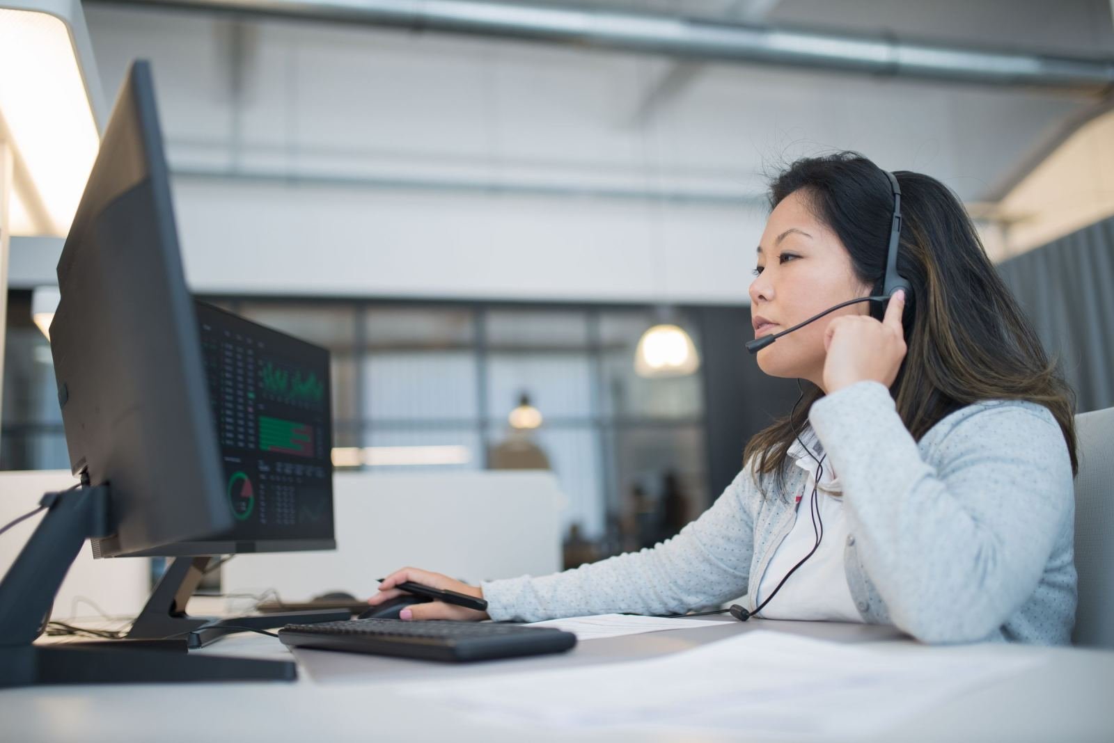 A woman wearing a headset sits at a computer in an office.