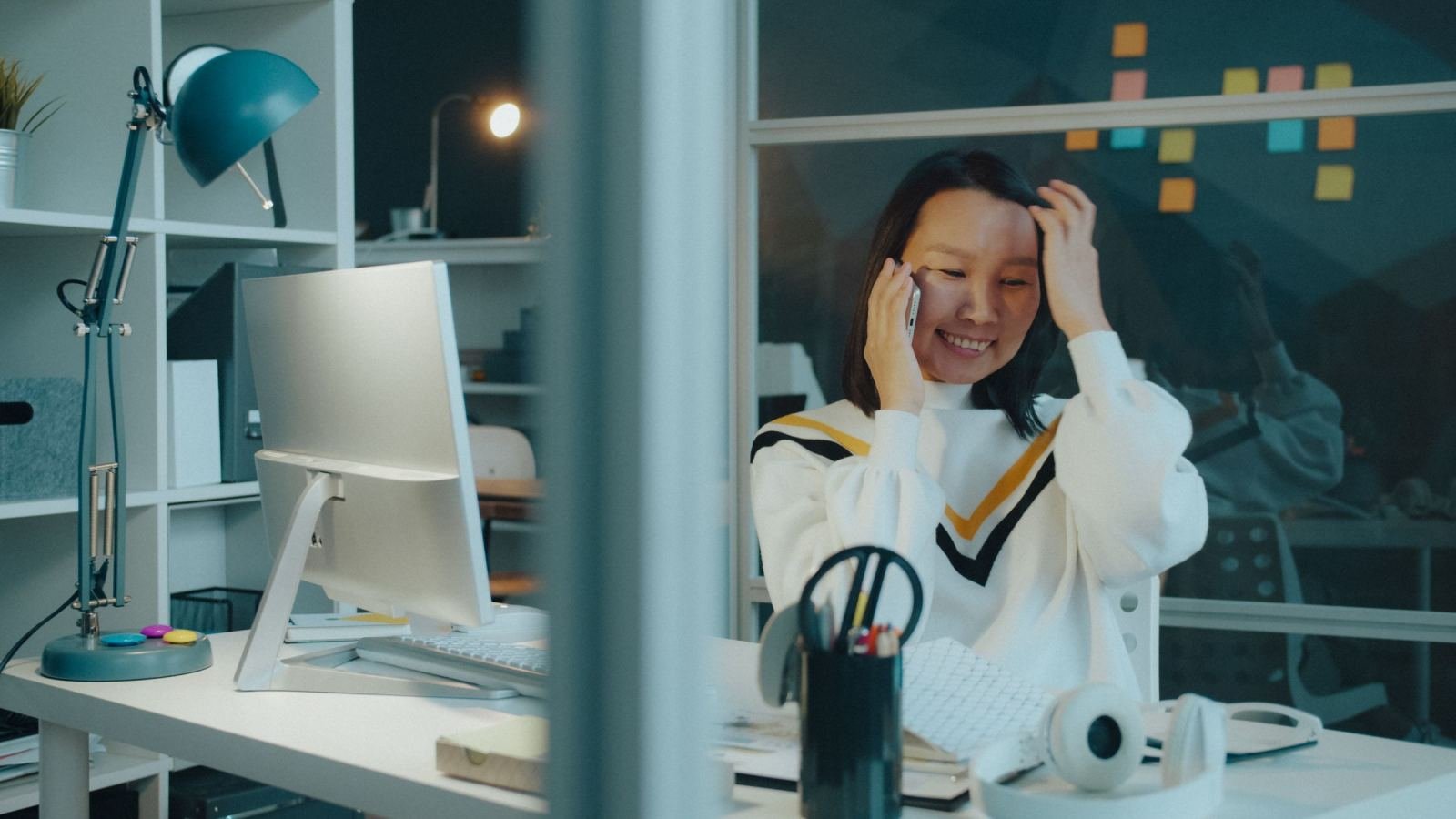 A smiling woman talks on a mobile phone while sitting at her office desk