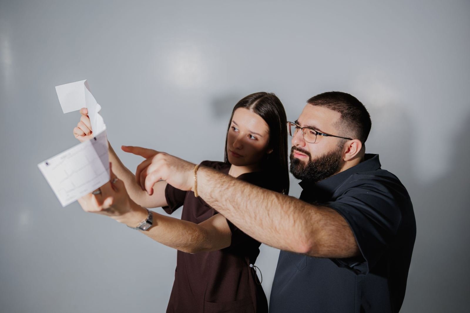 A man and woman review a folded white paper together against a grey background