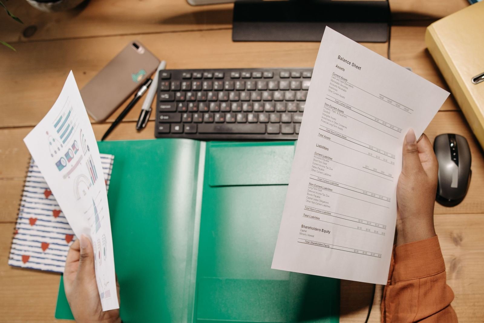 Hands holding financial balance sheets over a desk with a keyboard and mouse