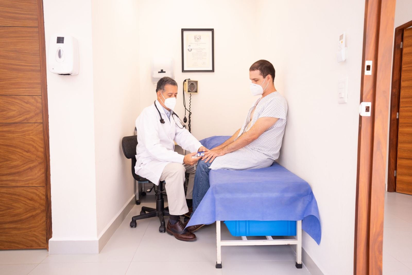 A physician wearing a white coat uses a pulse oximeter to check a patient's finger.