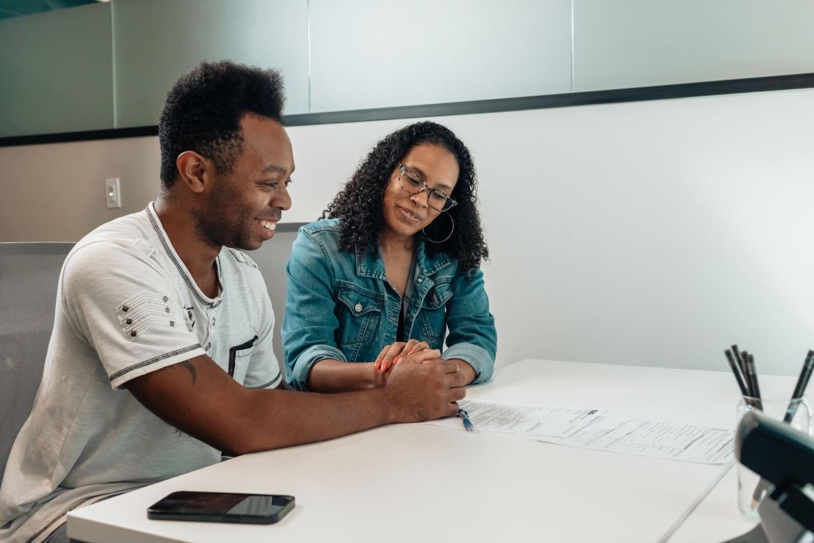 Two people, a man and a woman, sit at a white table looking over paperwork.