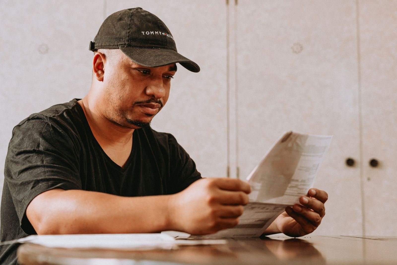 A person wearing a dark hat looks over papers at a desk