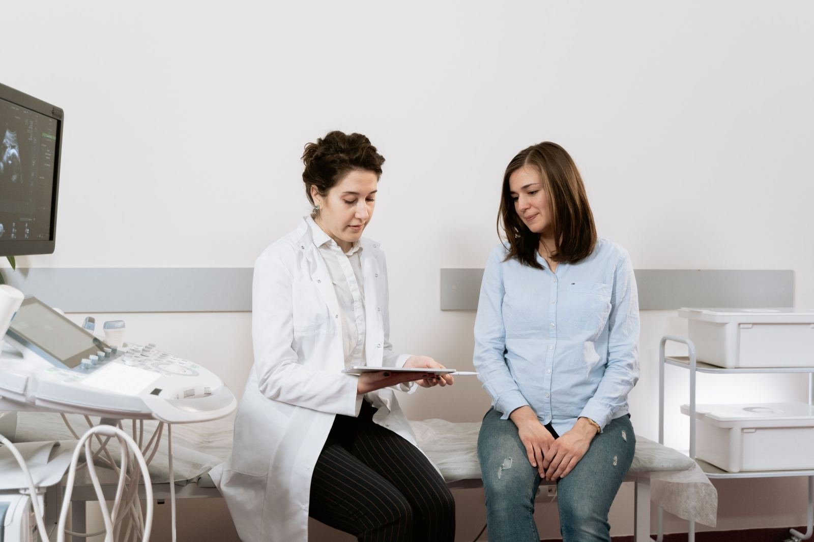 A doctor in a white coat-clad shows a tablet to a pregnant woman.