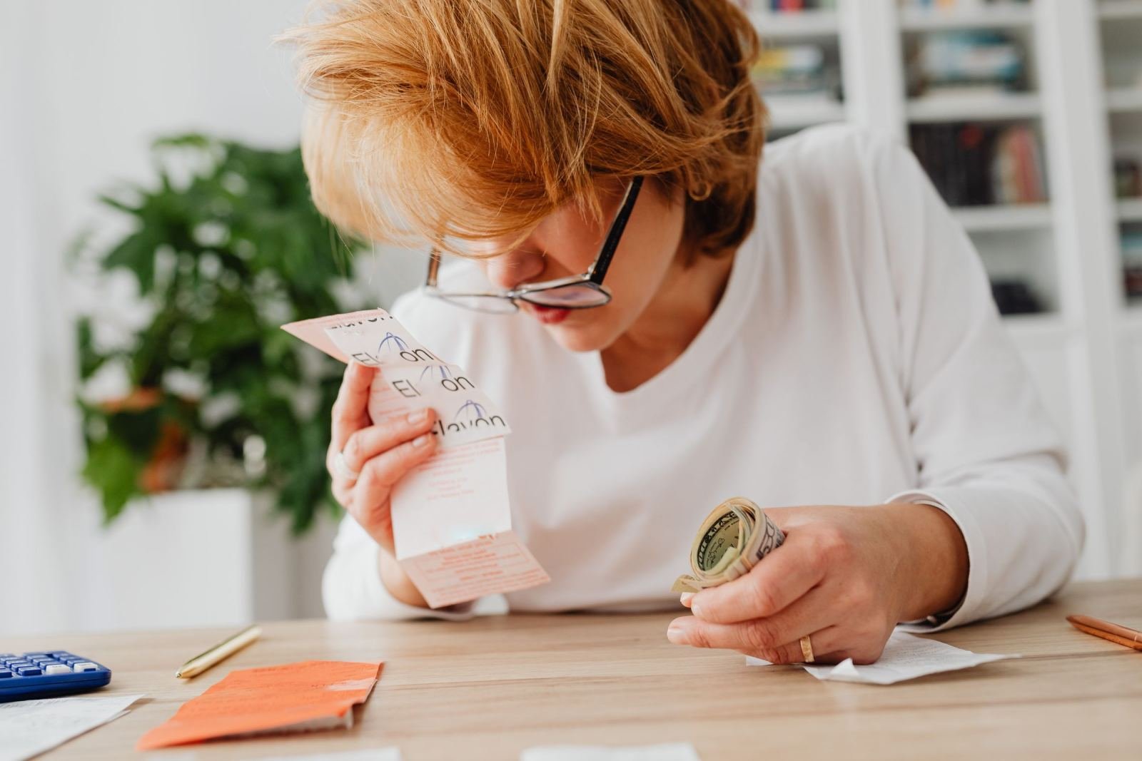 A woman looks at a receipt while holding a roll of cash at a table