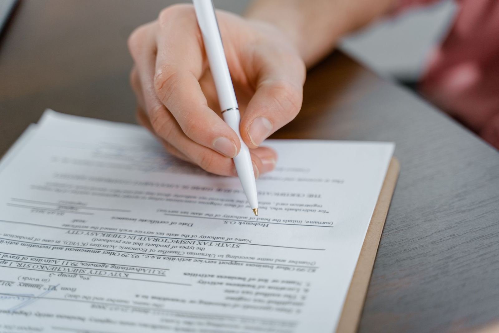 A person holds a white pen over a printed form on a clipboard