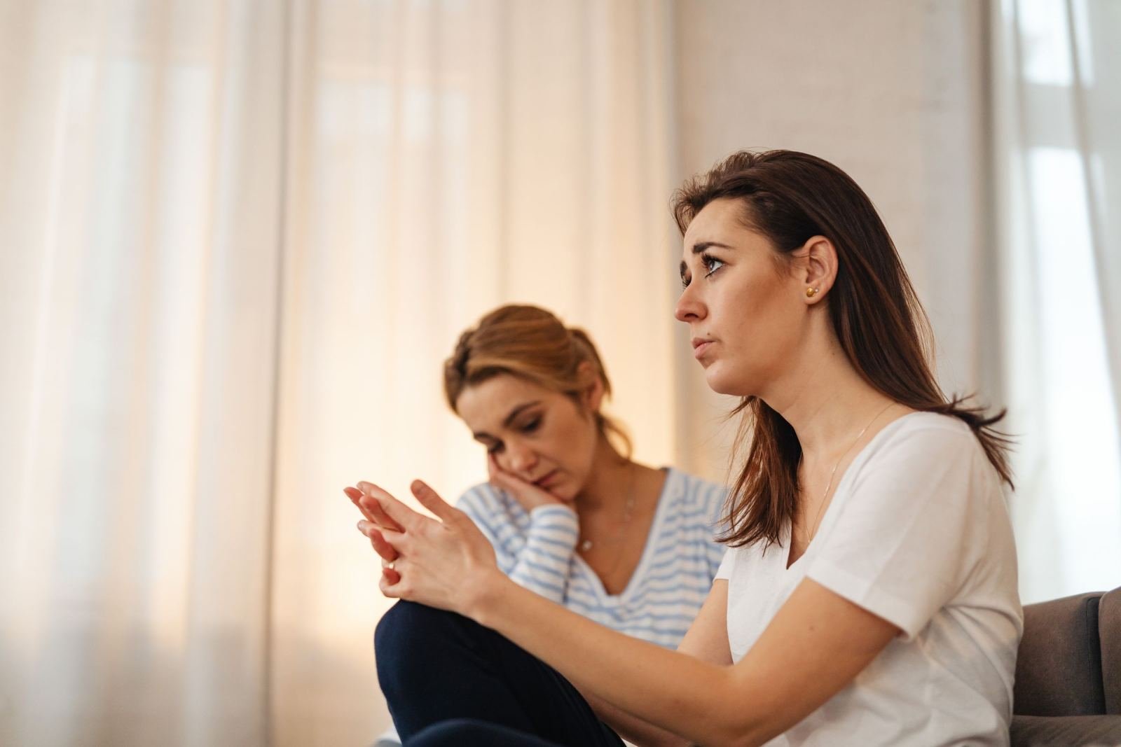 Two women sit together in a bright room, one speaking and gesturing while the other listens