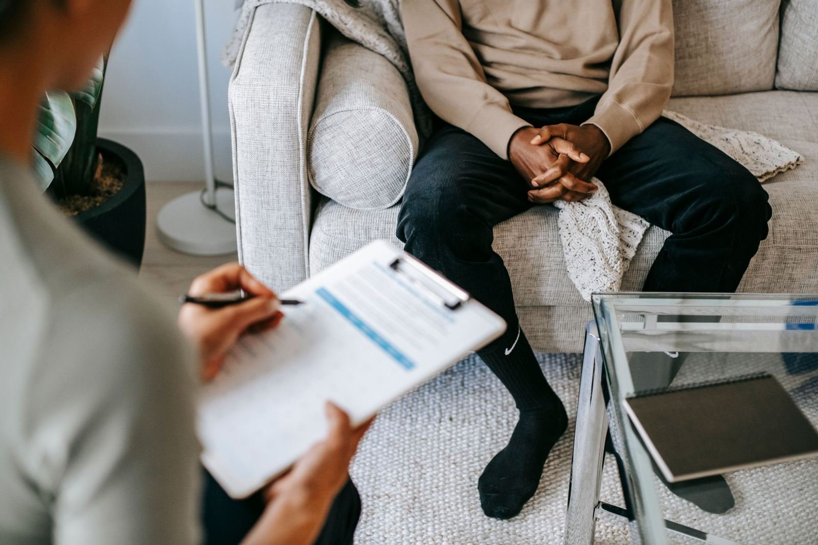 A therapist with a clipboard sits across from a man on a sofa