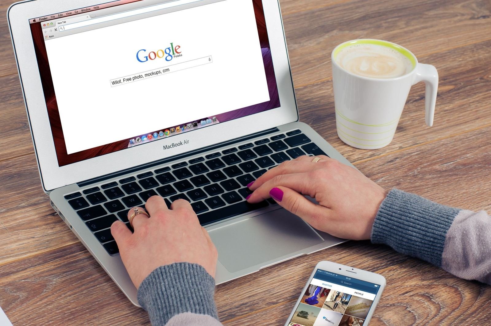 Image of hands typing on a laptop with a coffee mug and phone nearby.