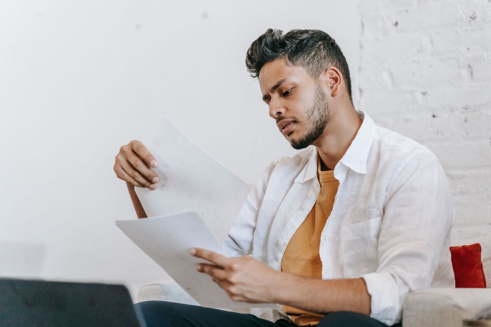 A man in a white shirt sits on a couch, going over some papers.