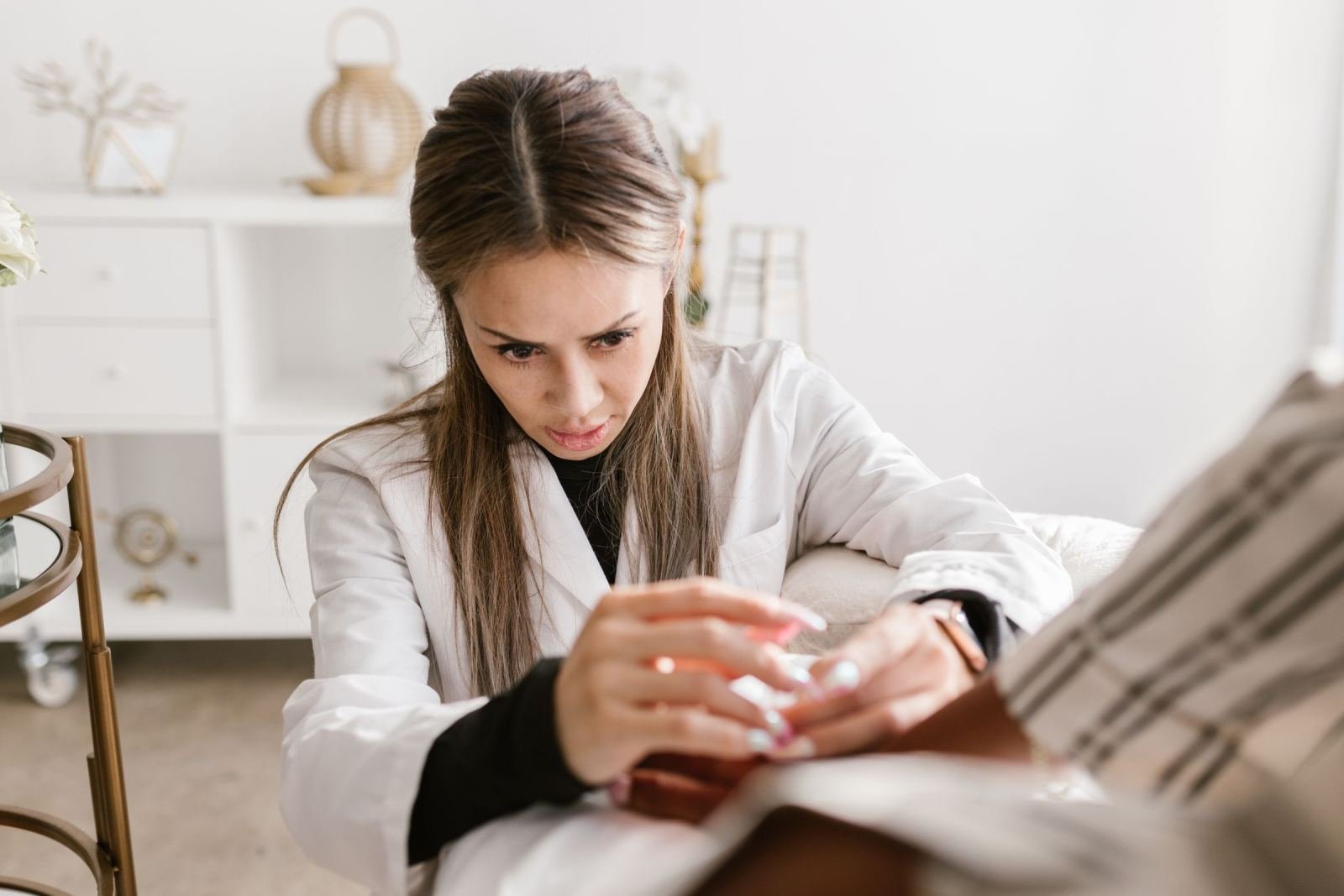 A doctor in a white coat takes a patient's hand in a well-lit room.