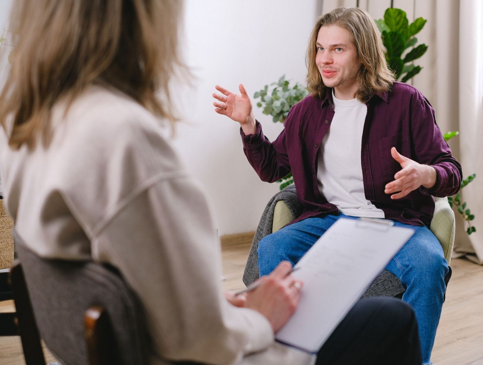 A man gestures while speaking to a counselor holding a clipboard
