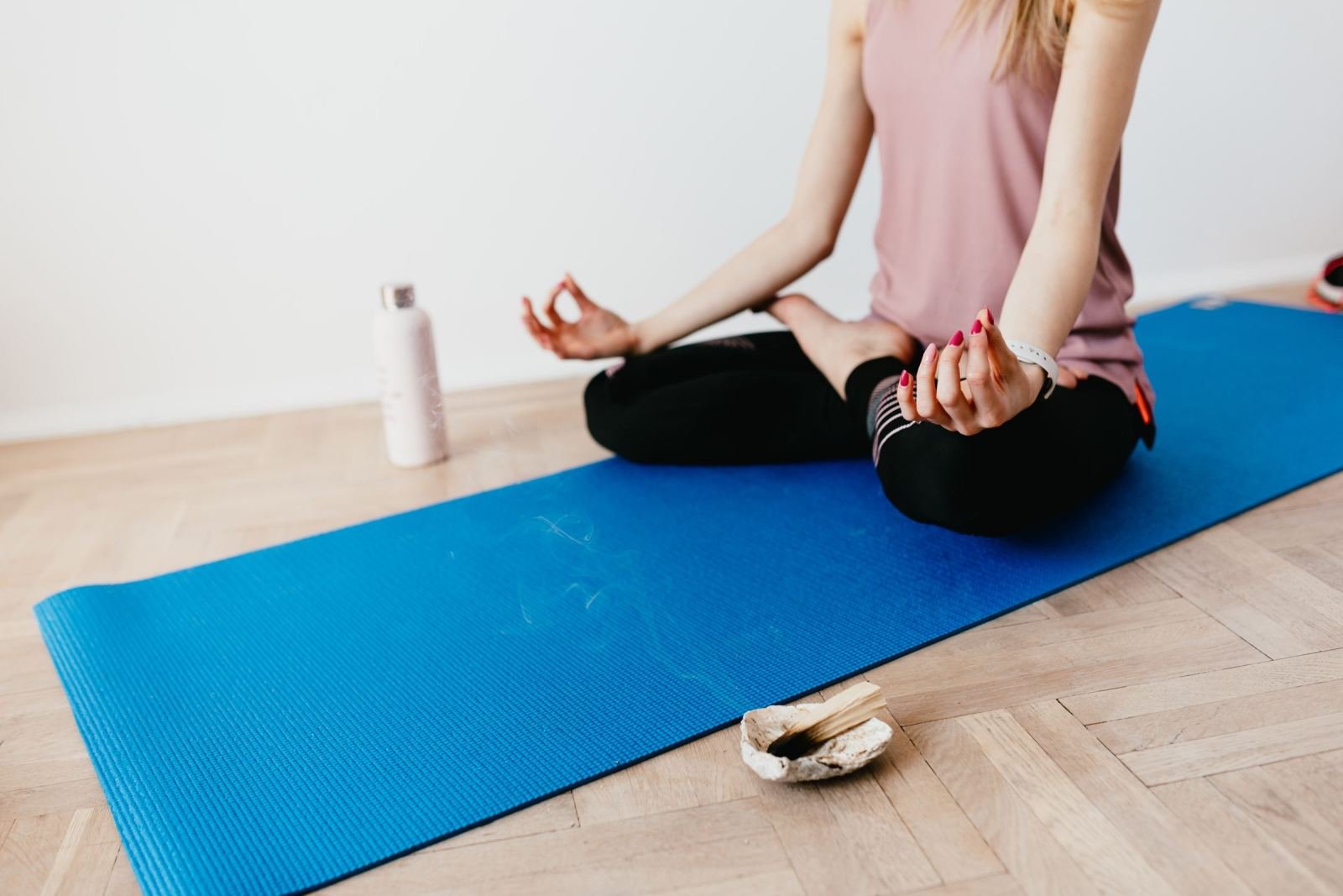 A person sits cross-legged on a blue yoga mat, meditating.