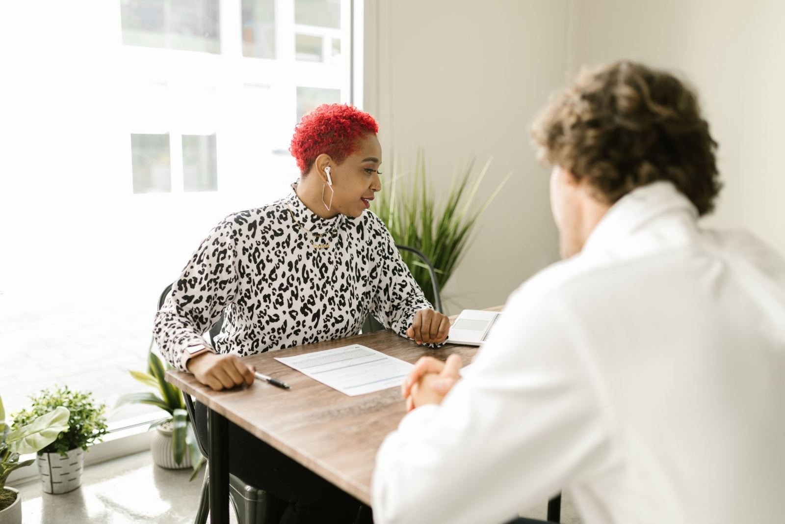 A red-haired woman talks to a man at a table covered with papers.