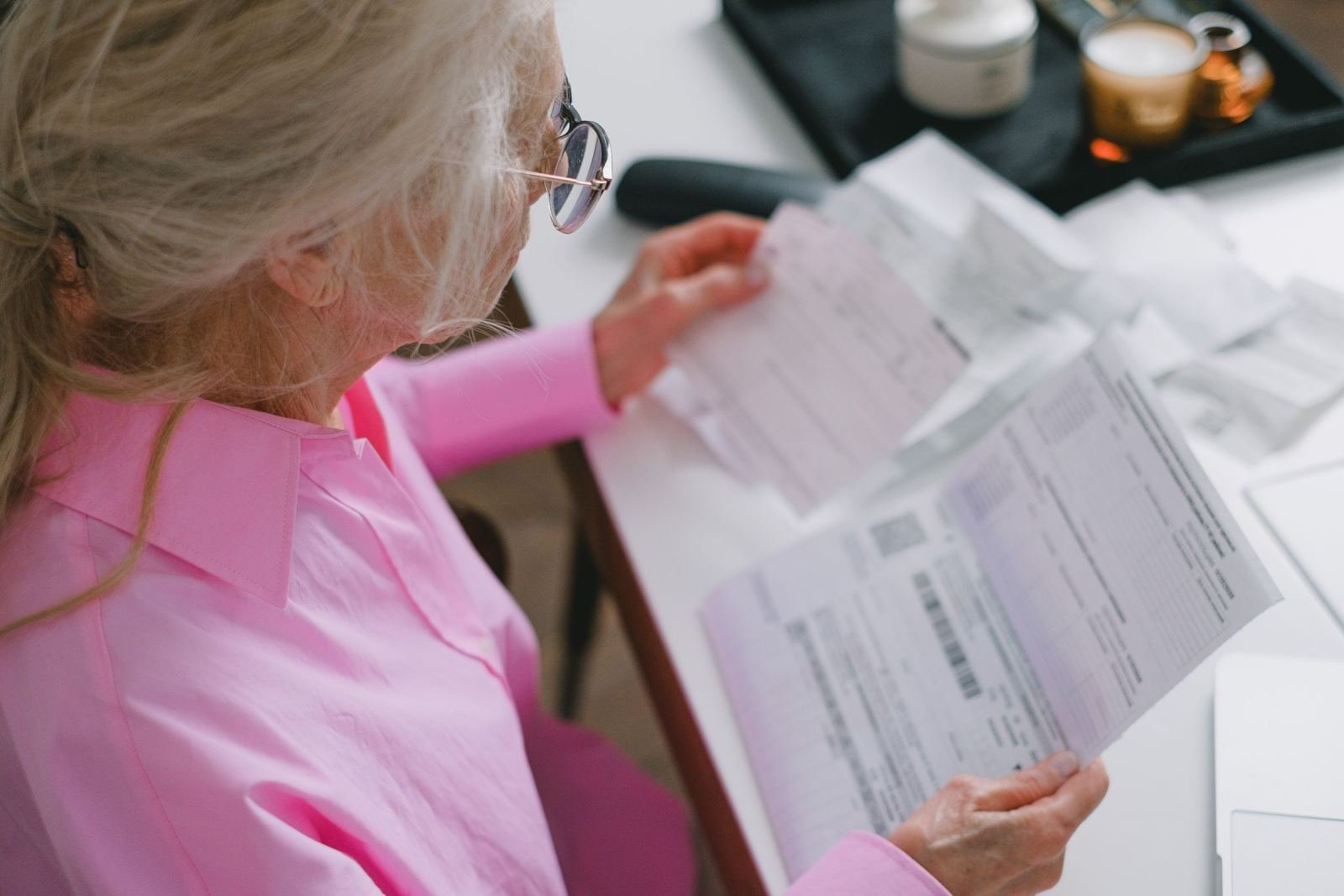 A woman wearing a pink shirt sits at a white desk. She looks over some printed papers.