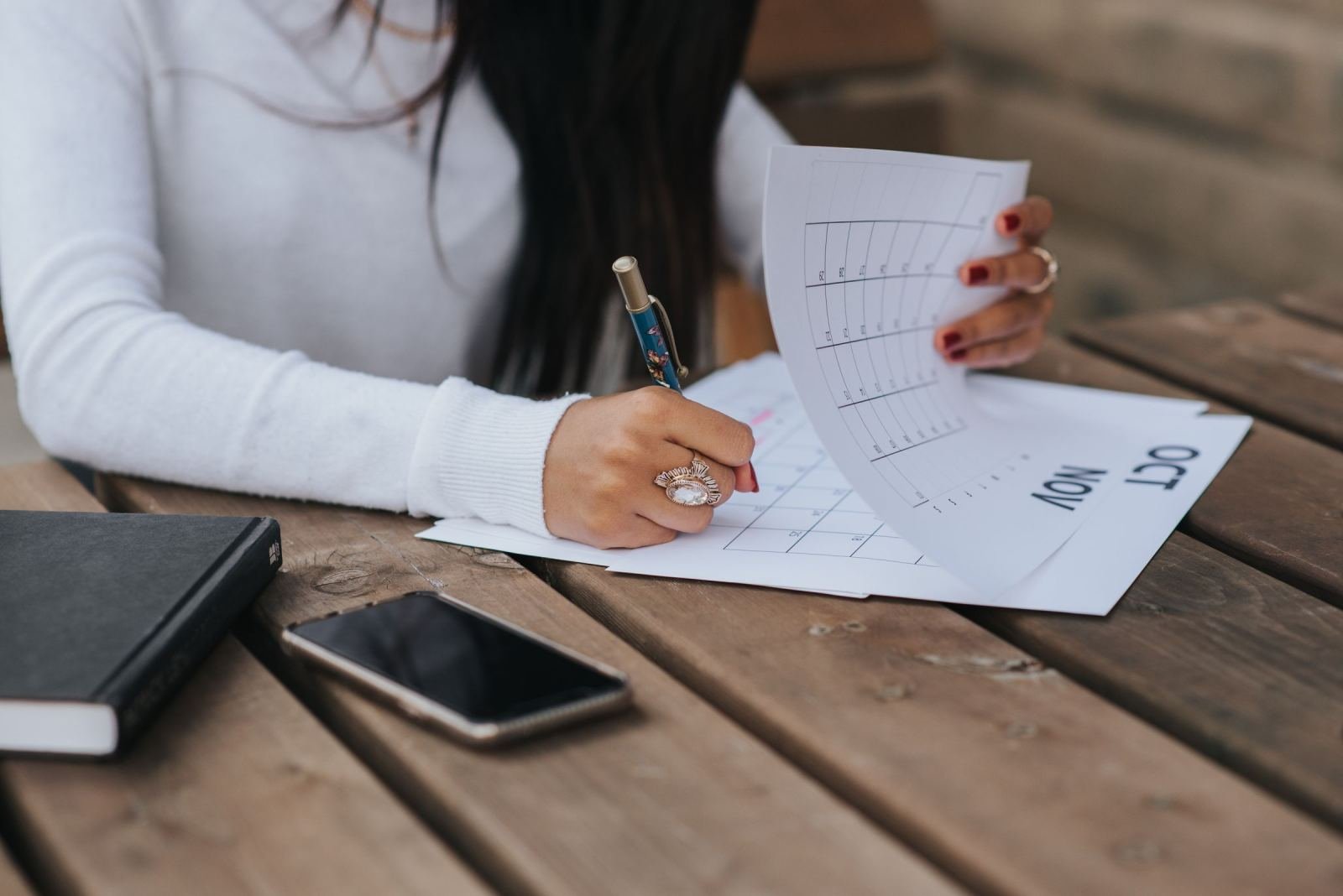 Someone in a white sweater marks dates on a paper calendar with a pen