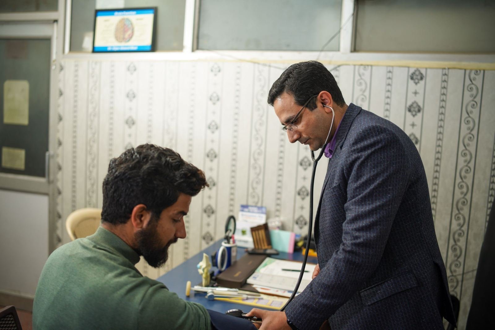 A doctor listens to a man's chest with a stethoscope in a well-lit office.