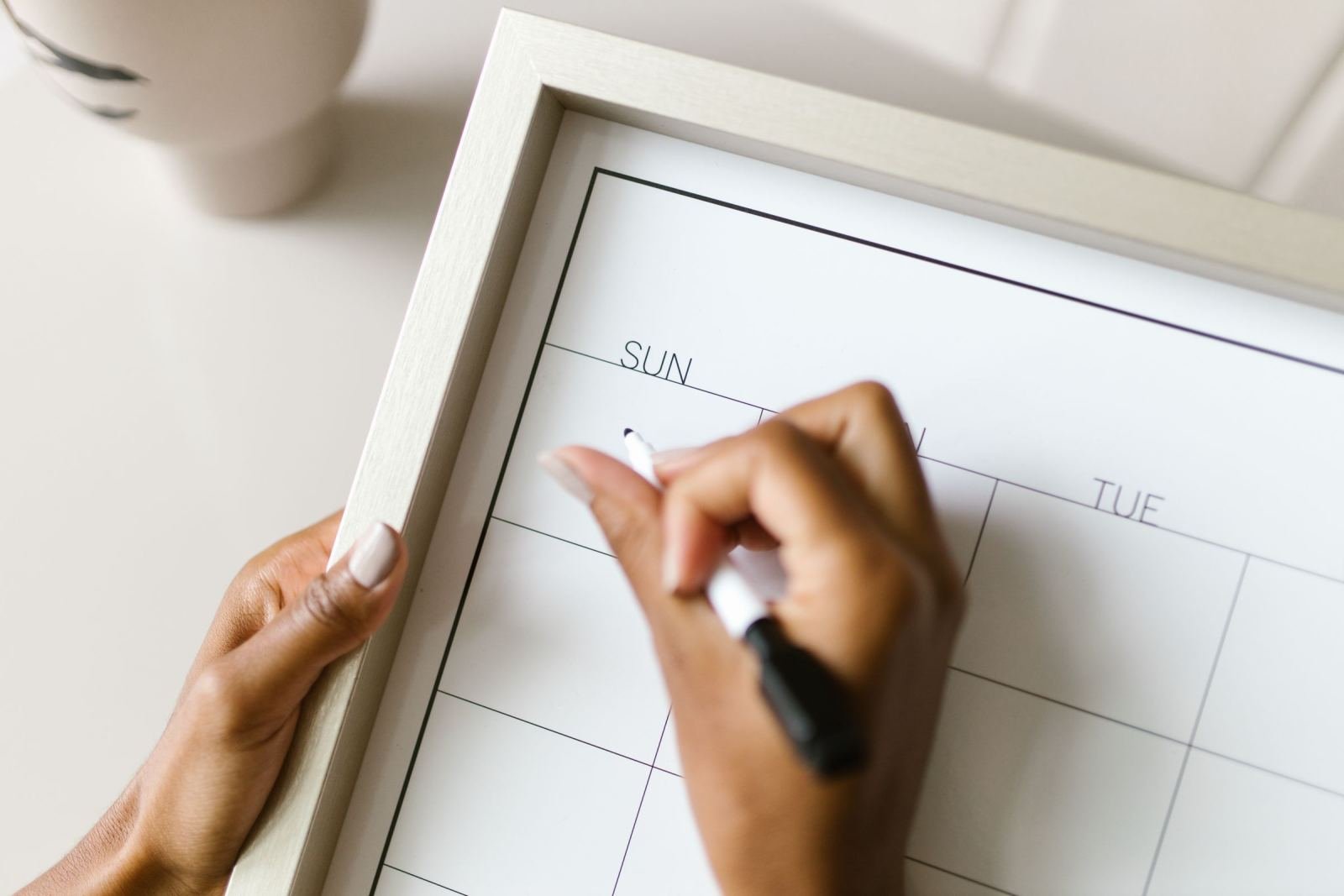 Hands using a black marker to write on a white dry-erase wall calendar